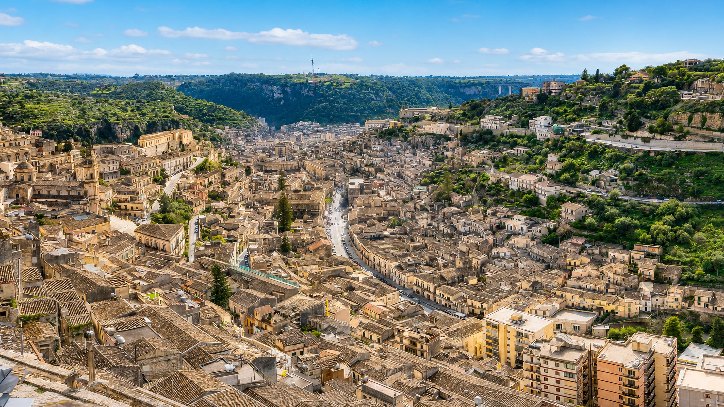 Modica's stone houses and tiled roofs packed across the Sicilian gorge beneath green ridges.