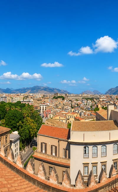 Rooftop view from Palermo Cathedral showing its Gothic spires above the city with mountains beyond under a blue sky