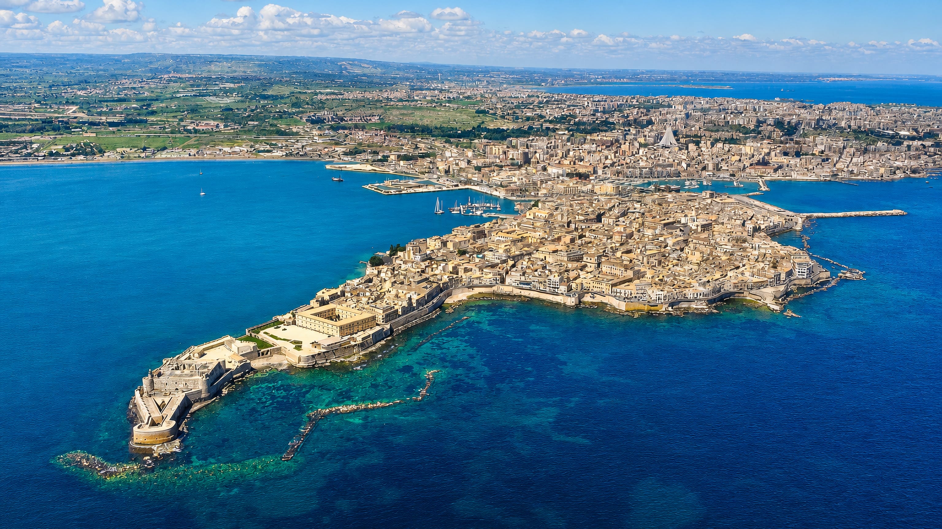 Aerial view of Siracusa's island of Ortigia ringed by turquoise sea, with Castello Maniace at its southern tip