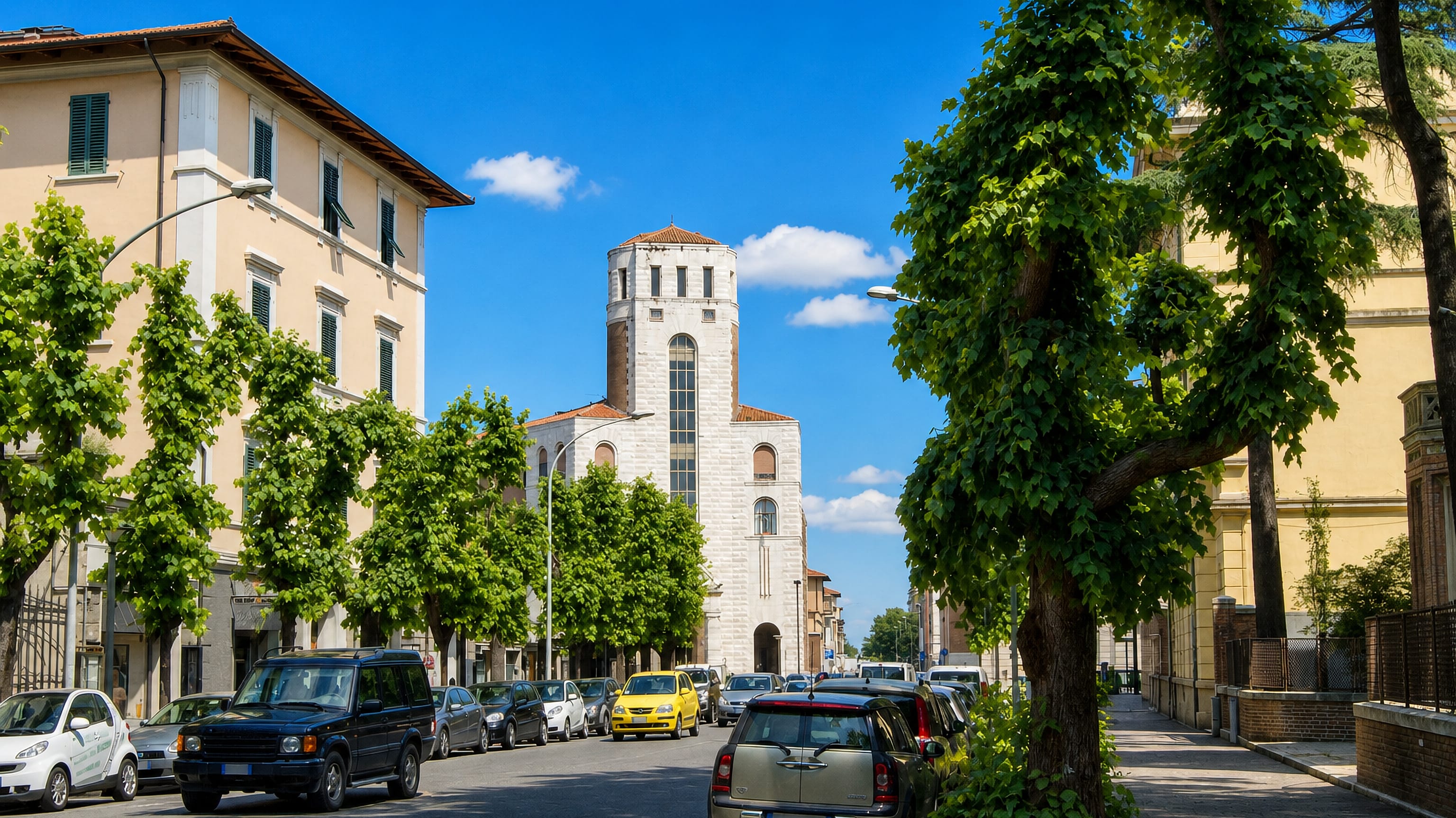 Tree-lined avenue in Porta Nuova, Grosseto, leading to a pale stone church with an octagonal bell tower.