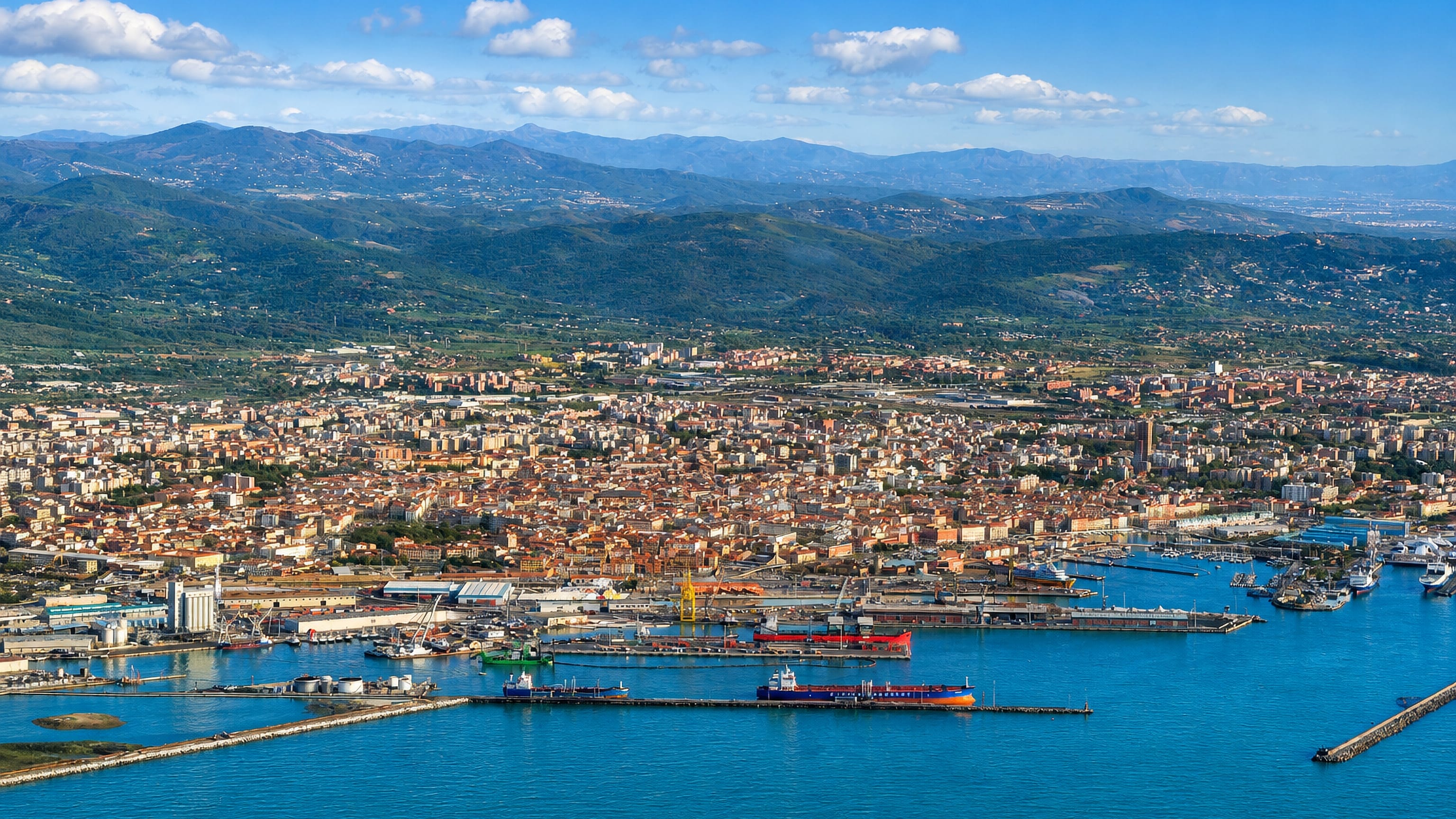 Aerial view of Livorno's commercial port, breakwaters and dense terracotta city with Tuscan hills behind
