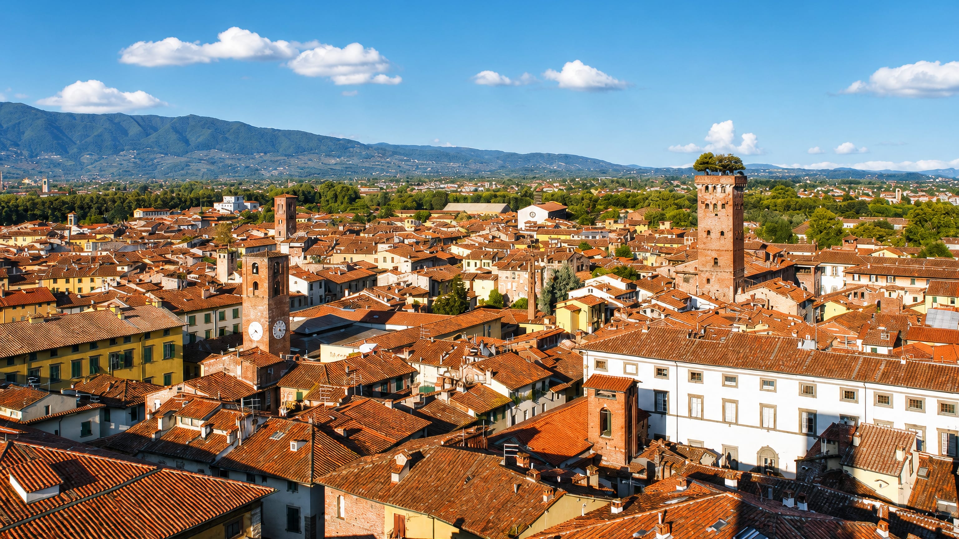 Lucca's terracotta rooftops from above, with the tree-topped Guinigi Tower and clock tower against the Tuscan hills.