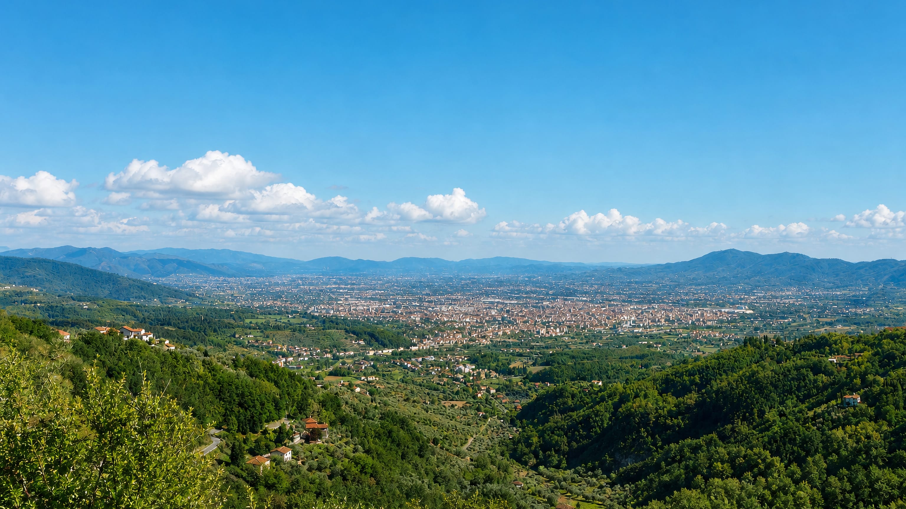 Pistoia and the Tuscan plain seen from wooded Apennine foothills under a clear blue sky.
