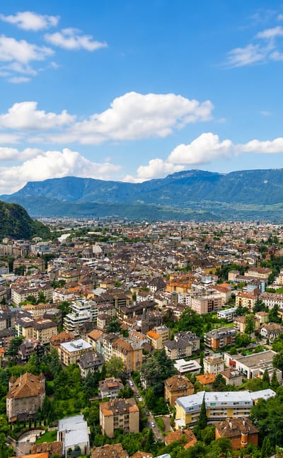 Bolzano nestled in the Adige valley surrounded by Dolomite mountains under a partly cloudy sky
