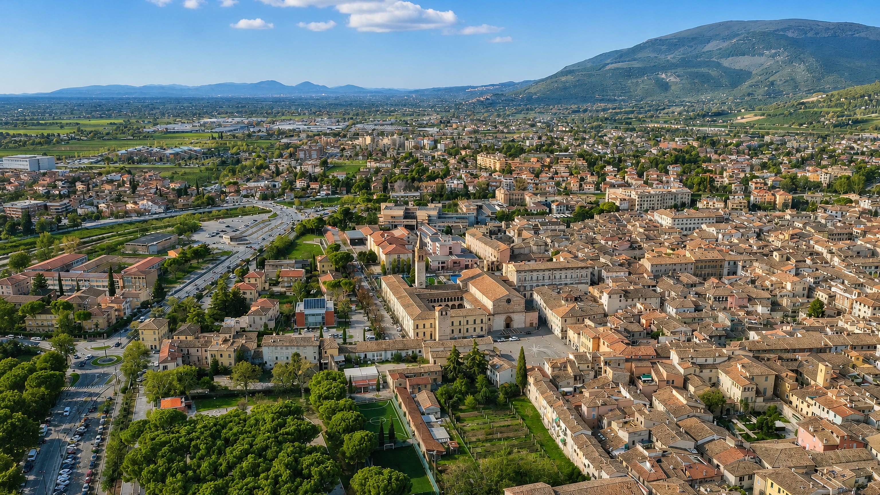 Aerial view over Foligno's terracotta rooftops and central piazza on the Umbrian plain below the Apennine foothills.