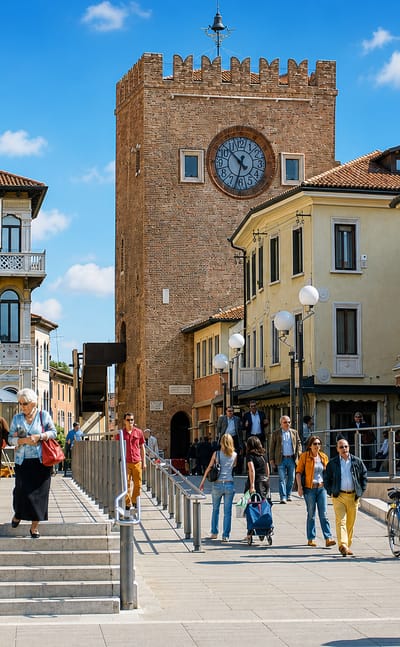 Piazza Erminio Ferretto in Mestre with the medieval Torre dell'Orologio clock tower and pastel Venetian buildings on a sunny day.