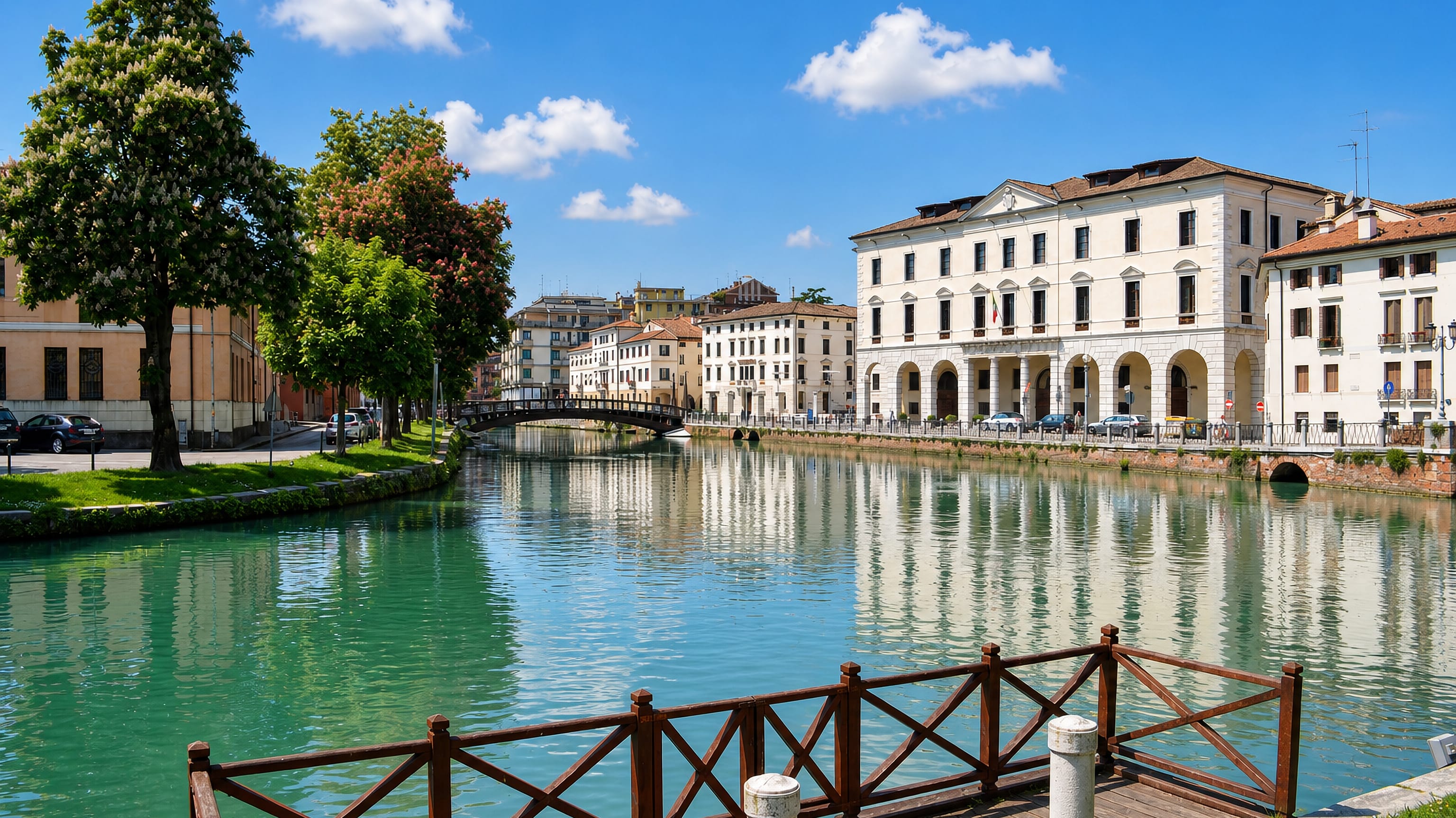 The Sile river in Treviso lined with arcaded palazzi, leafy banks and a footbridge reflected in green water.