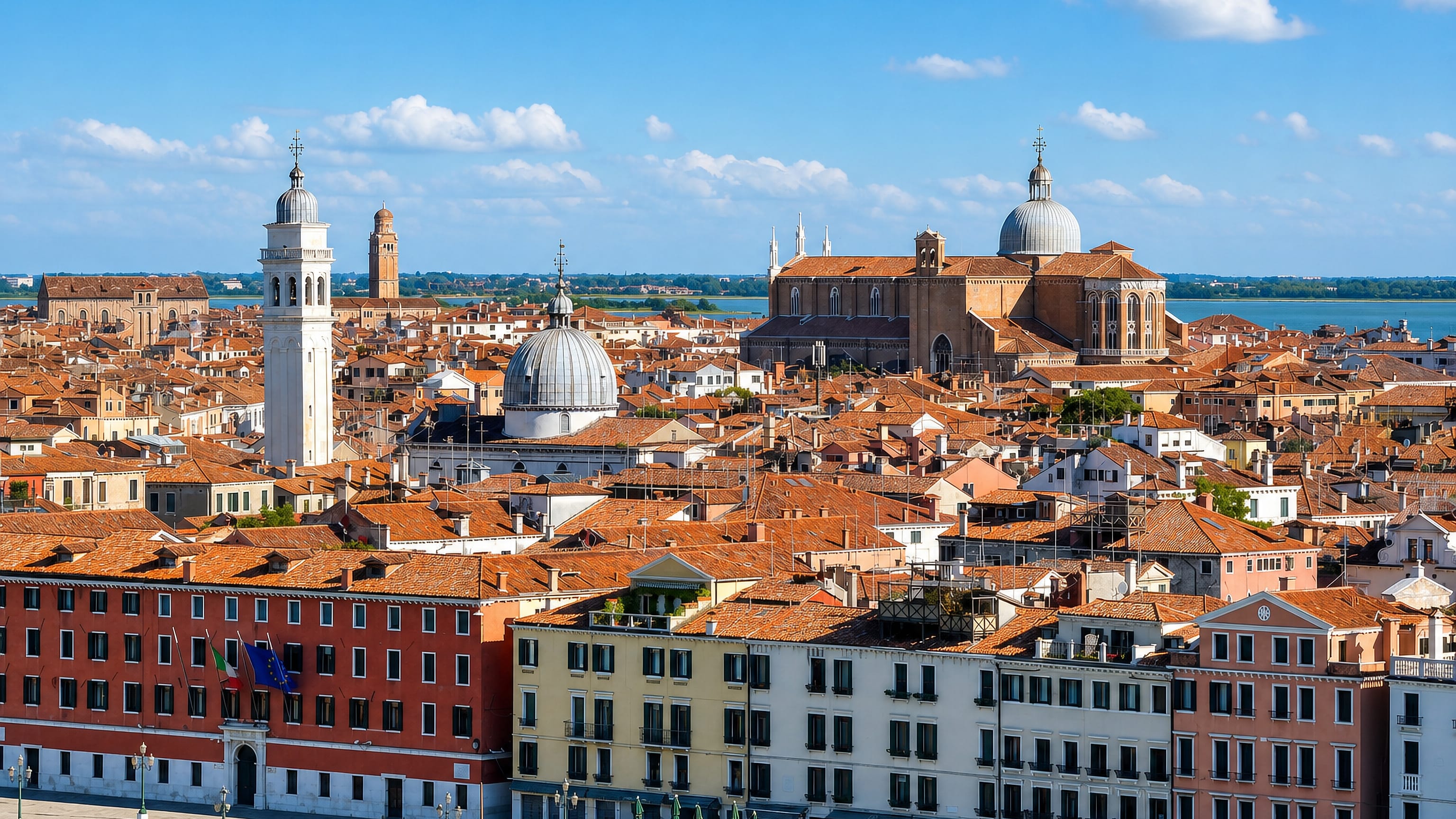 Terracotta rooftops, a leaning campanile and a domed basilica over Venice's Castello district and lagoon.
