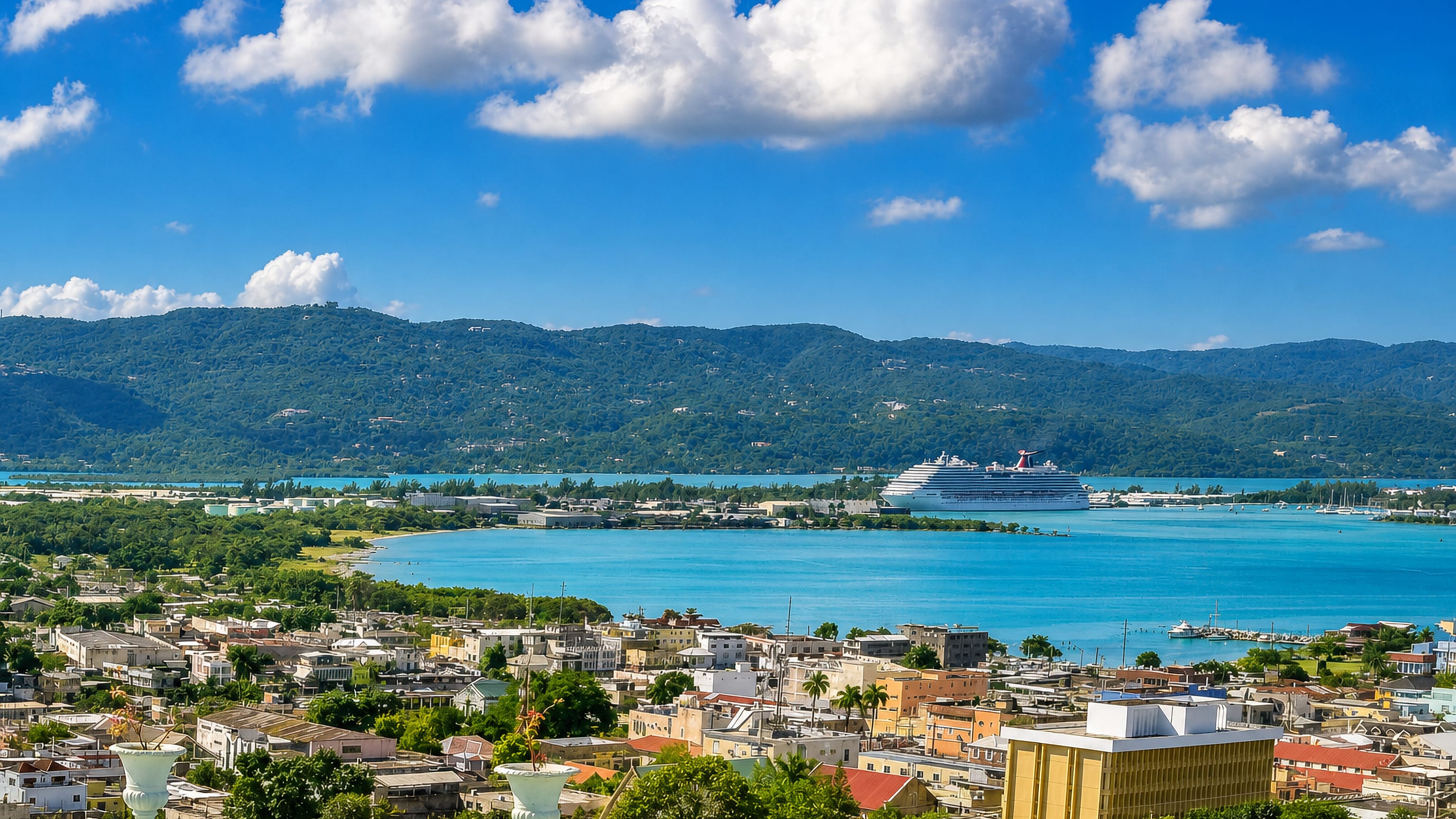 Montego Bay, Jamaica, from the hills, with turquoise water, a docked cruise ship and green hills behind.