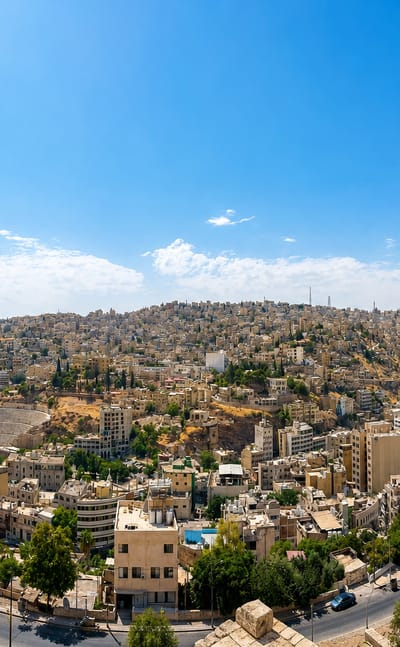 Panorama of Amman's pale stone buildings covering the hills with the ancient Roman Theatre visible below.