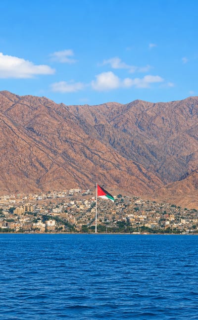 Aqaba, Jordan, on the Red Sea with the giant Aqaba flagpole and city below rugged brown mountains.