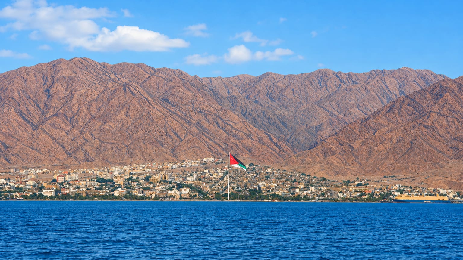 Aqaba, Jordan, on the Red Sea with the giant Aqaba flagpole and city below rugged brown mountains.