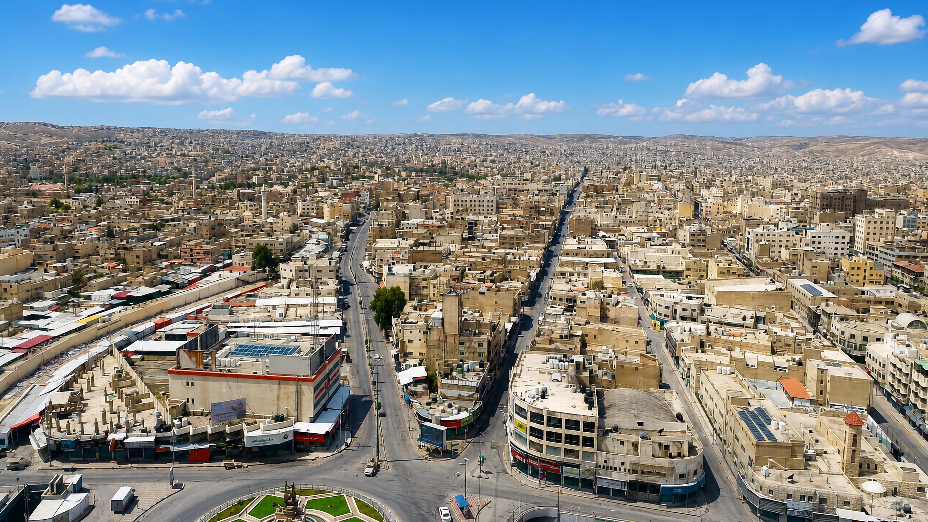 Dense pale-stone rooftops, a monument roundabout and arid hills stretching across Zarqa, Jordan.