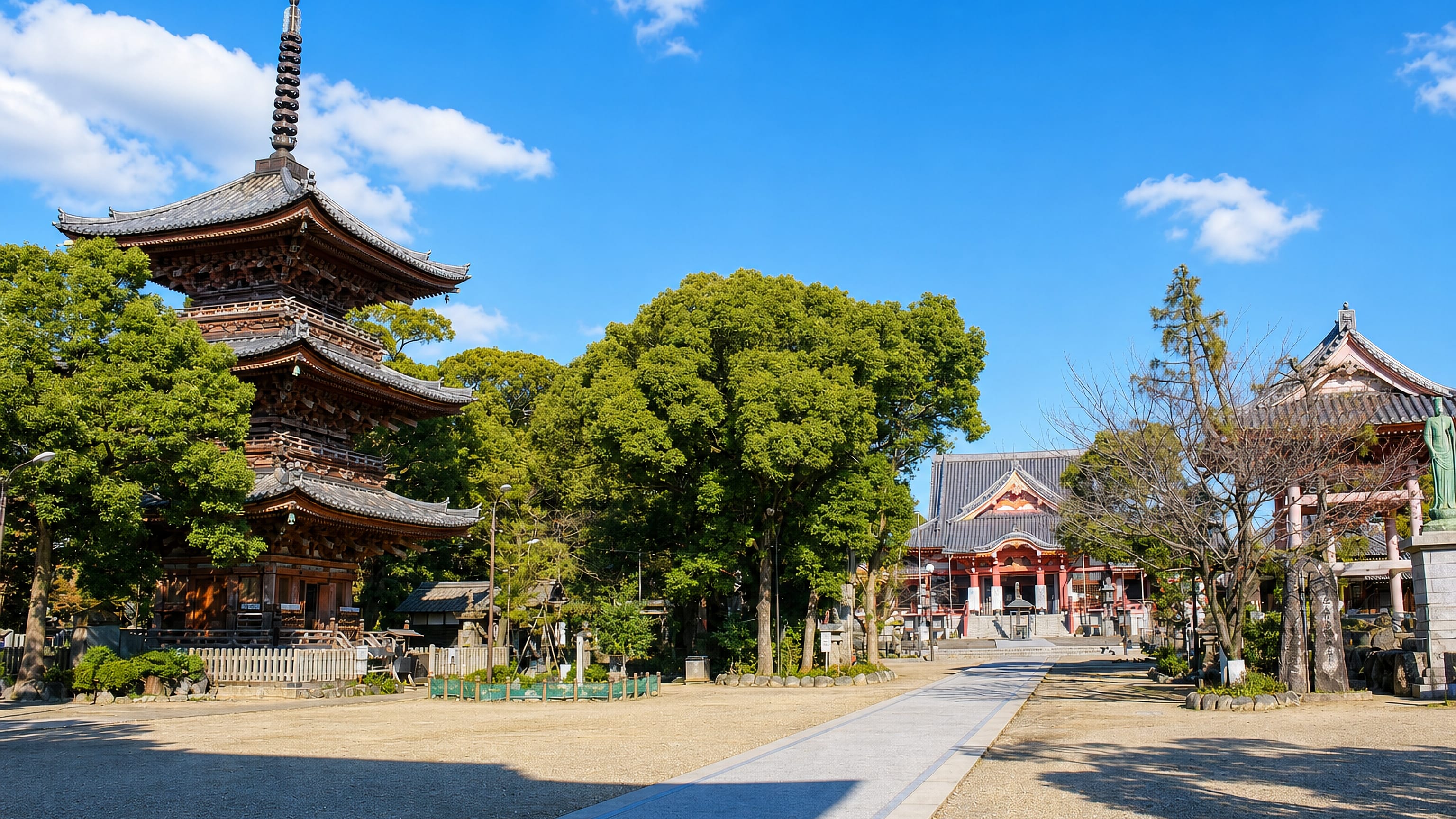 A three-storey wooden pagoda and red-painted temple hall in a gravel precinct in Ama, Aichi, Japan.