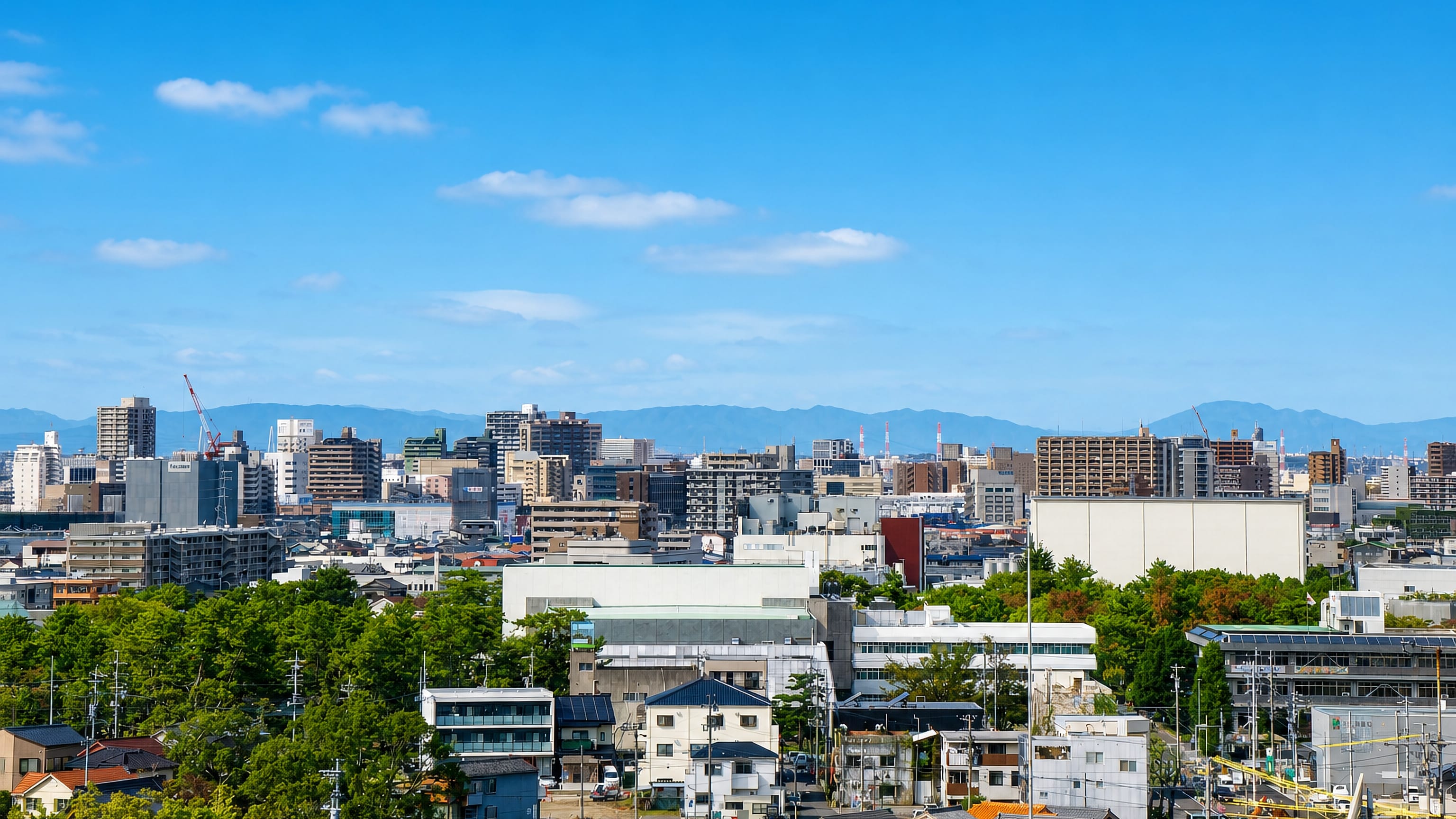 Mid-rise offices and apartment towers of central Anjo with low mountains on the horizon.