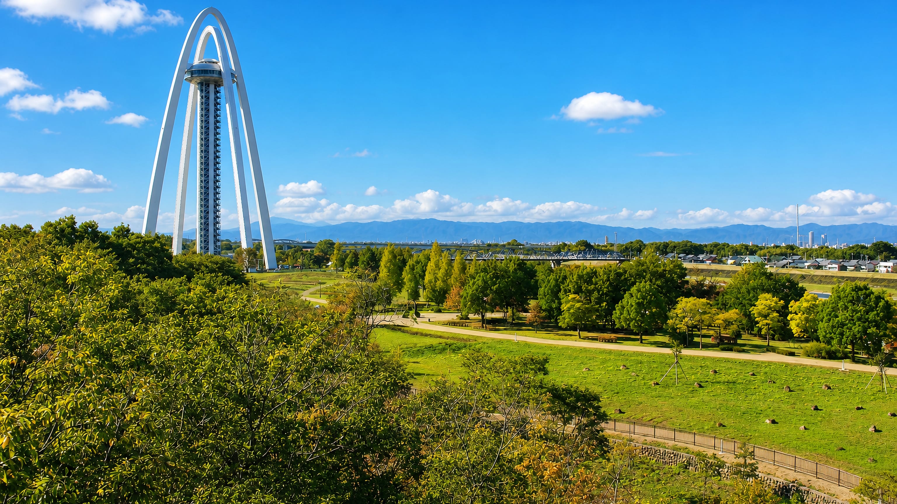 The Twin Arch 138 tower rising over riverside parkland in Ichinomiya, Japan, with mountains beyond.
