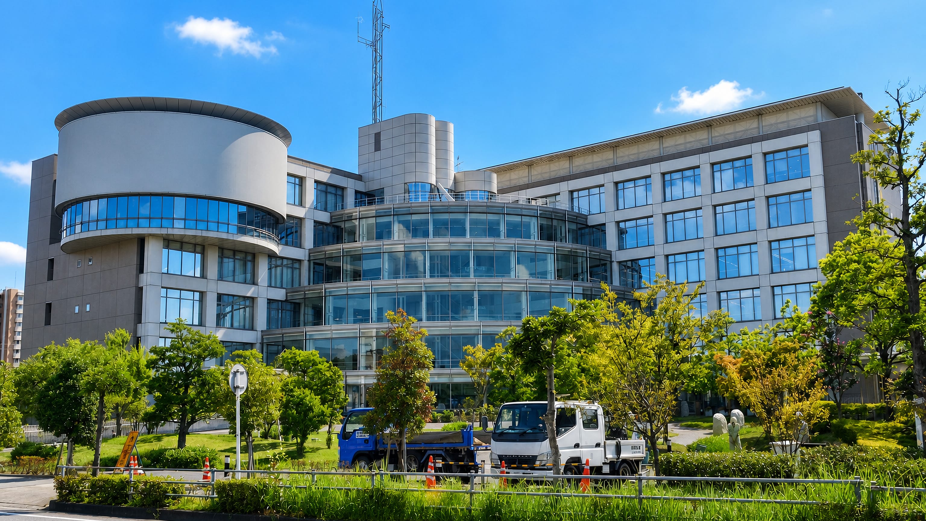 A modern glass-and-steel civic building in Ōbu, Aichi, framed by street trees under a clear sky.