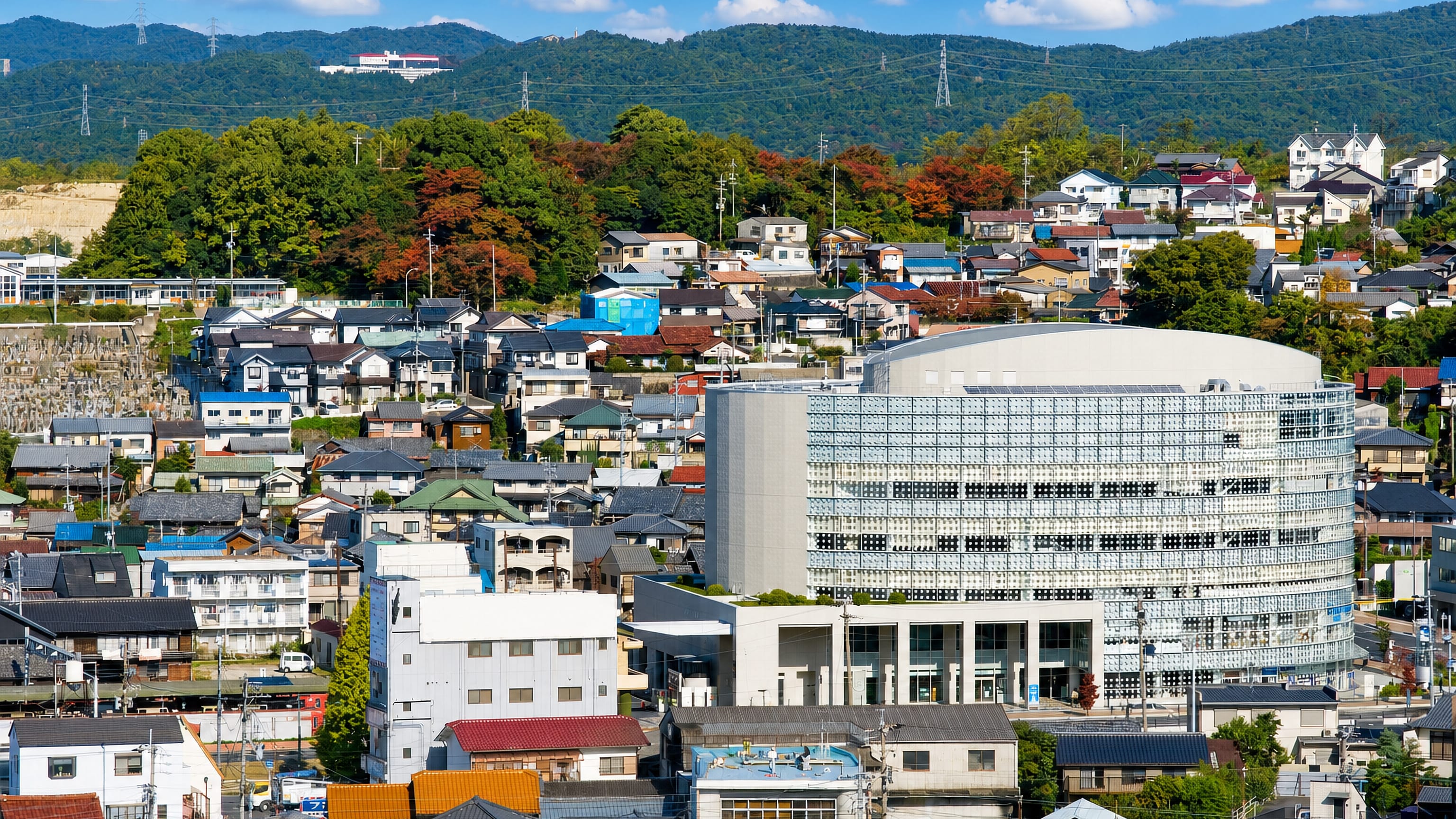 Seto, Japan, dense hillside housing and a curved glass civic building below forested Aichi hills.