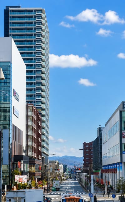 Street view in Toyota, Japan, past the KiTARA complex and COMO Square shopping buildings under a blue sky.