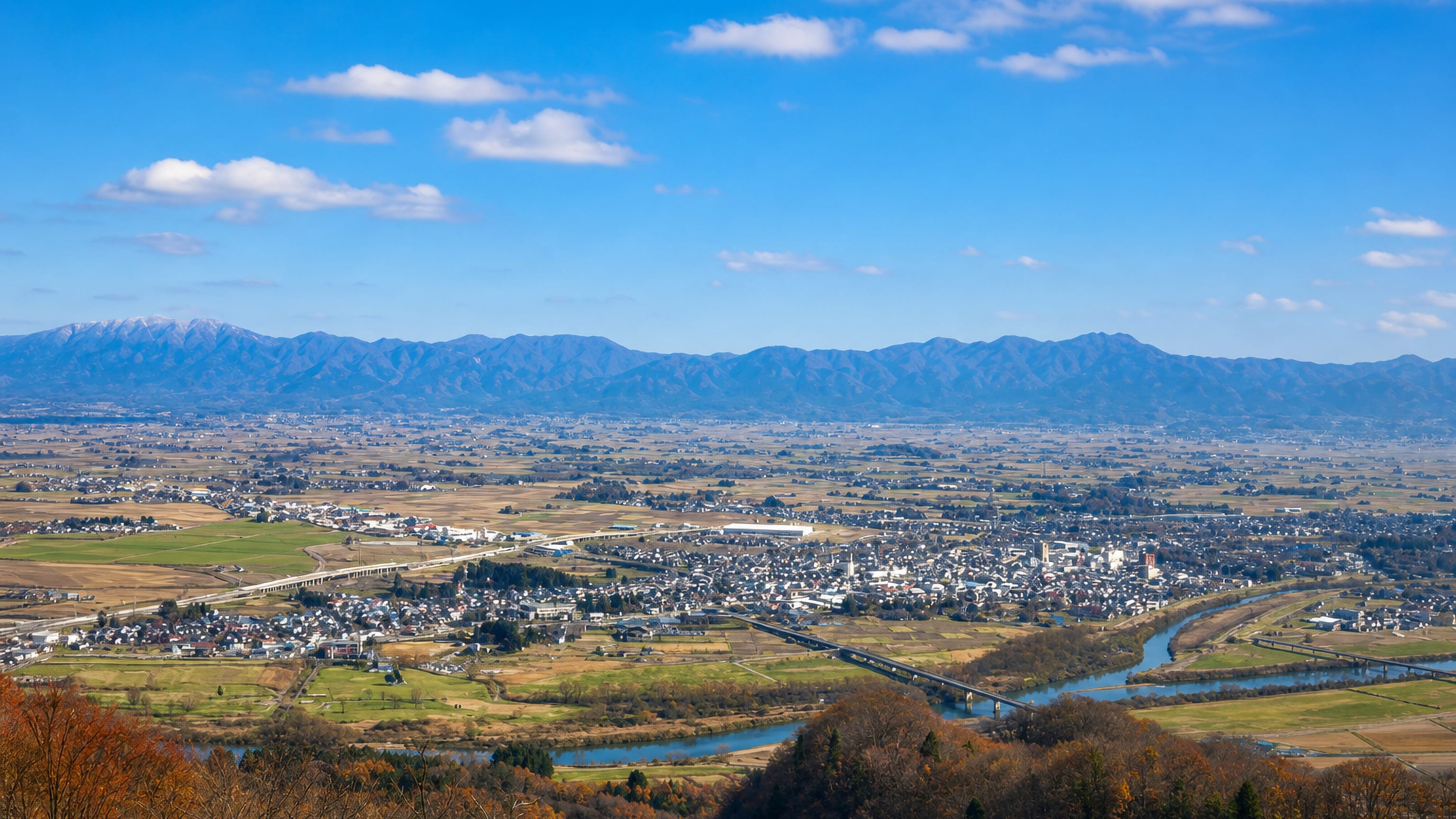 Daisen in Akita seen from the hills, its riverside town spreading across the Yokote basin below distant mountains.