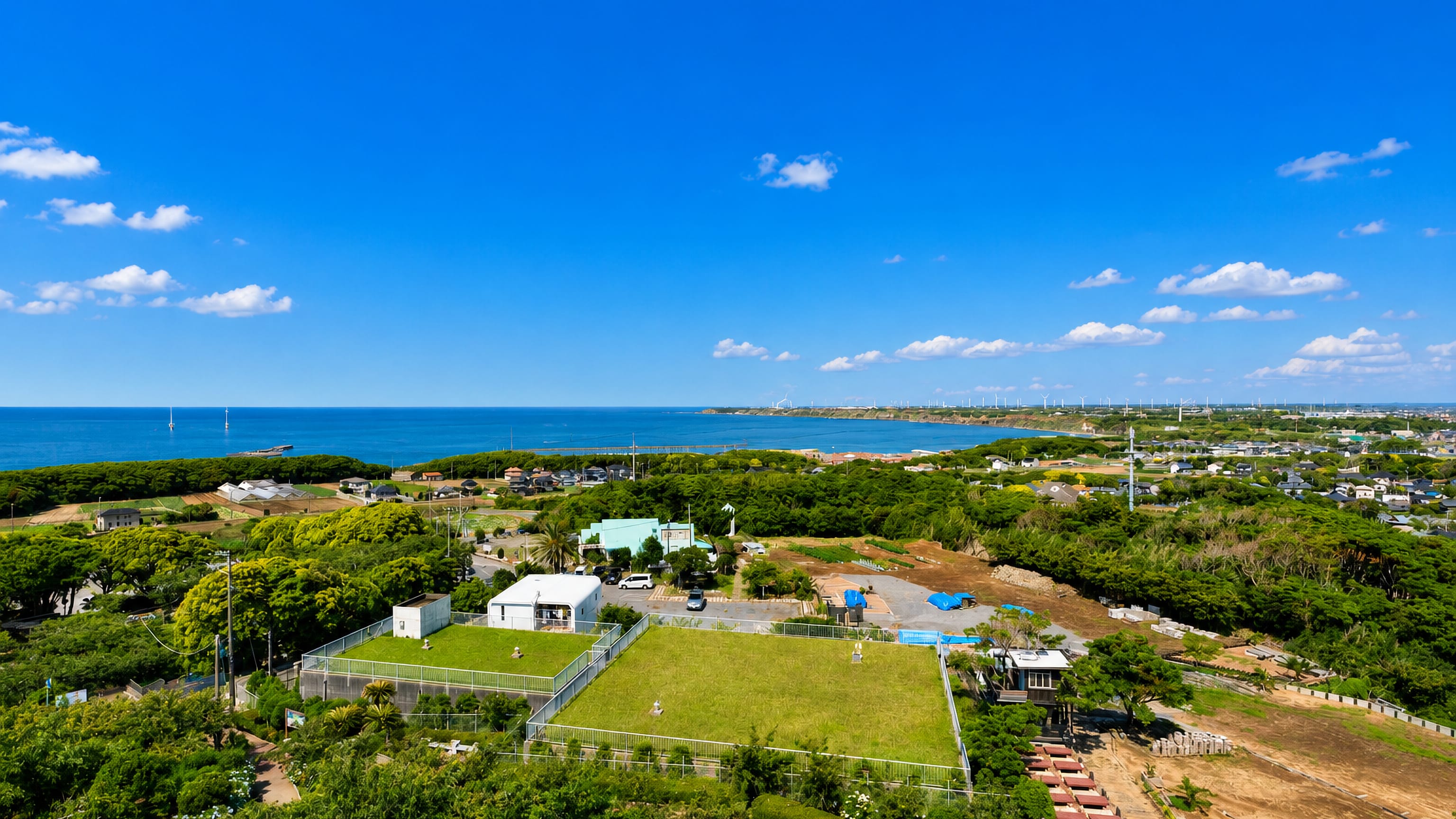 Coastal fields and wooded plain at Choshi, Japan, with the Pacific and offshore wind turbines on the horizon.