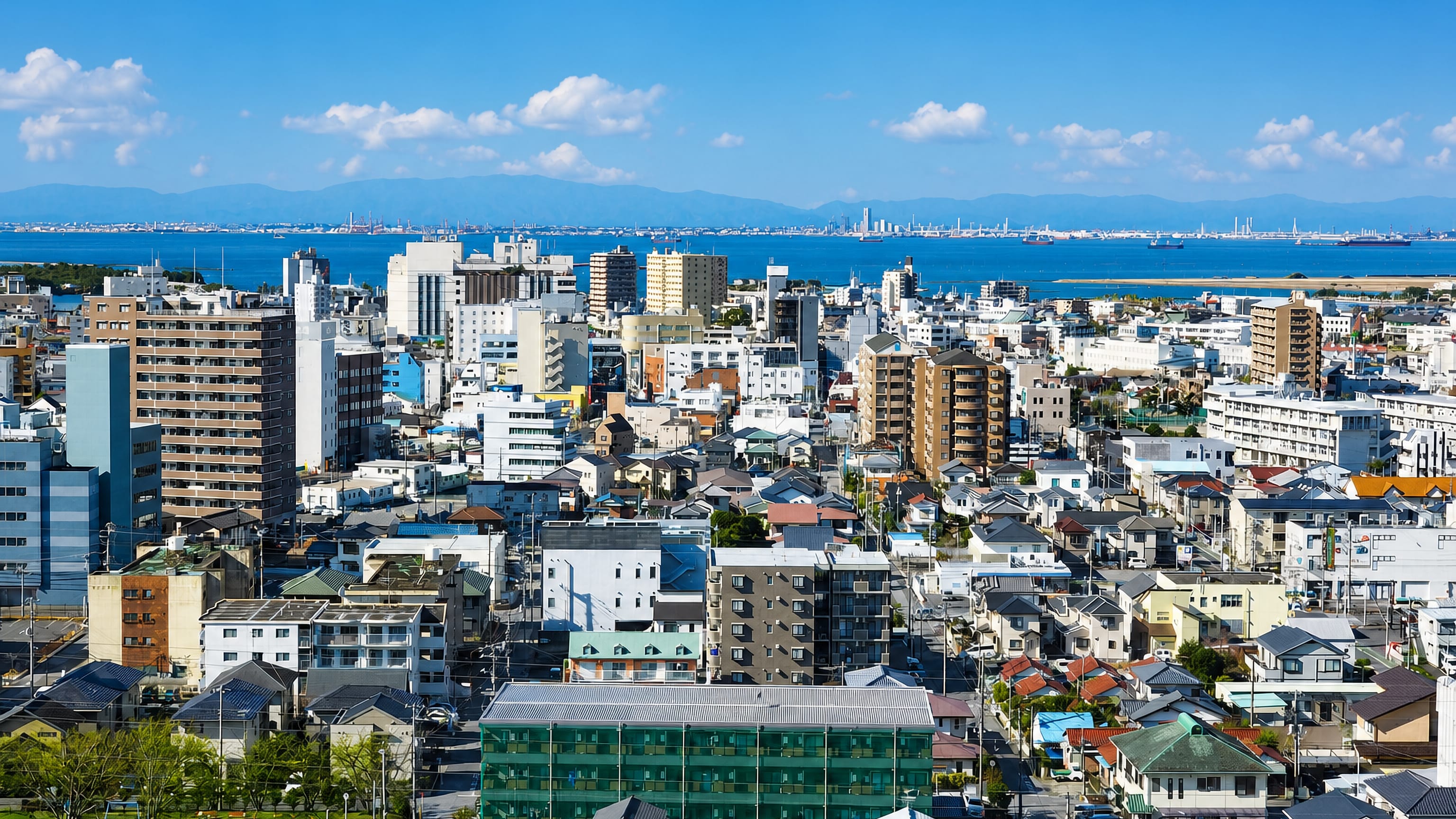 Low-rise Kisarazu spreading toward Tokyo Bay, with the industrial far shore and mountains on the horizon.