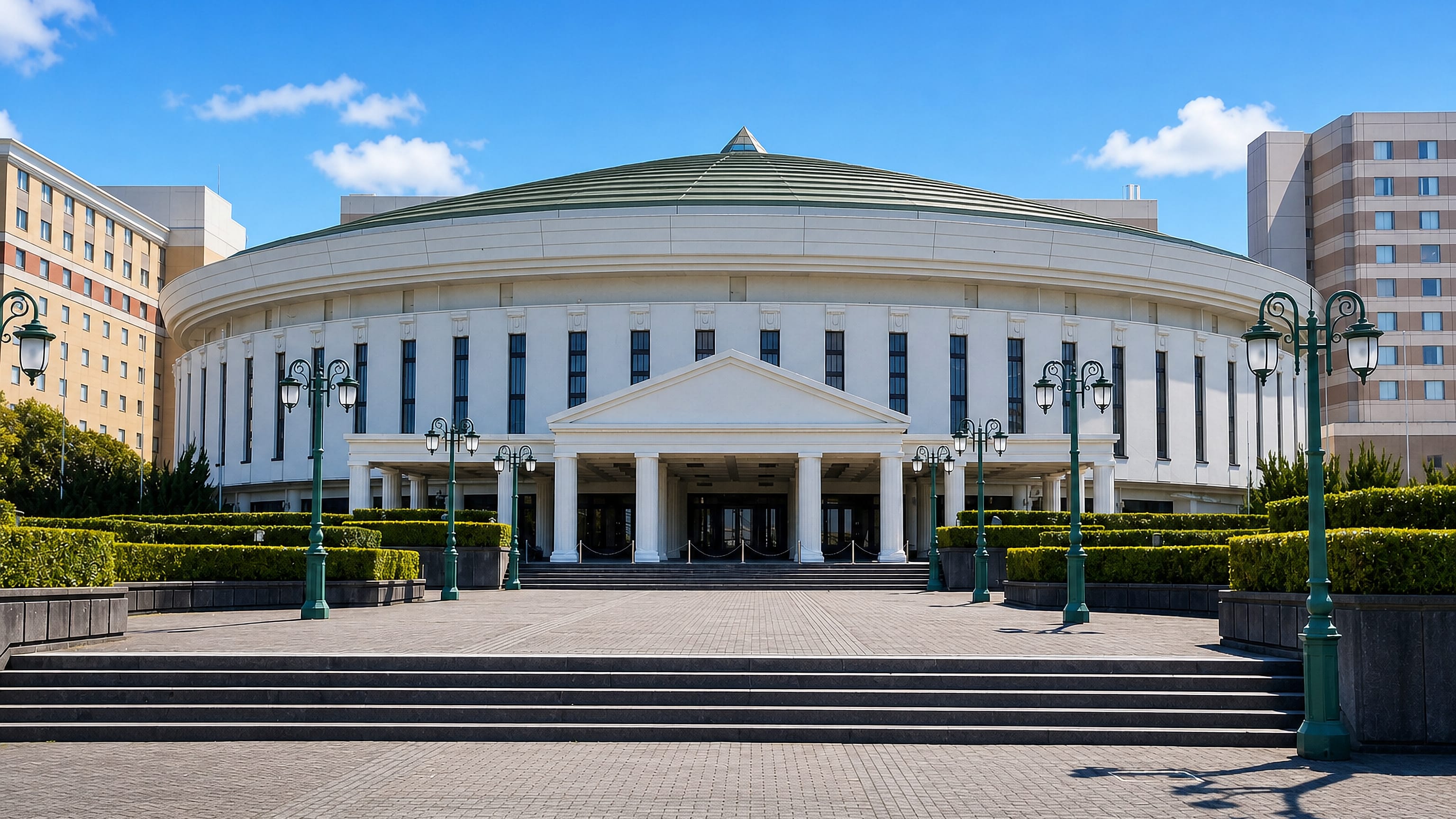 Domed white civic hall with colonnaded entrance and green roof in Urayasu, Japan, seen across its plaza.