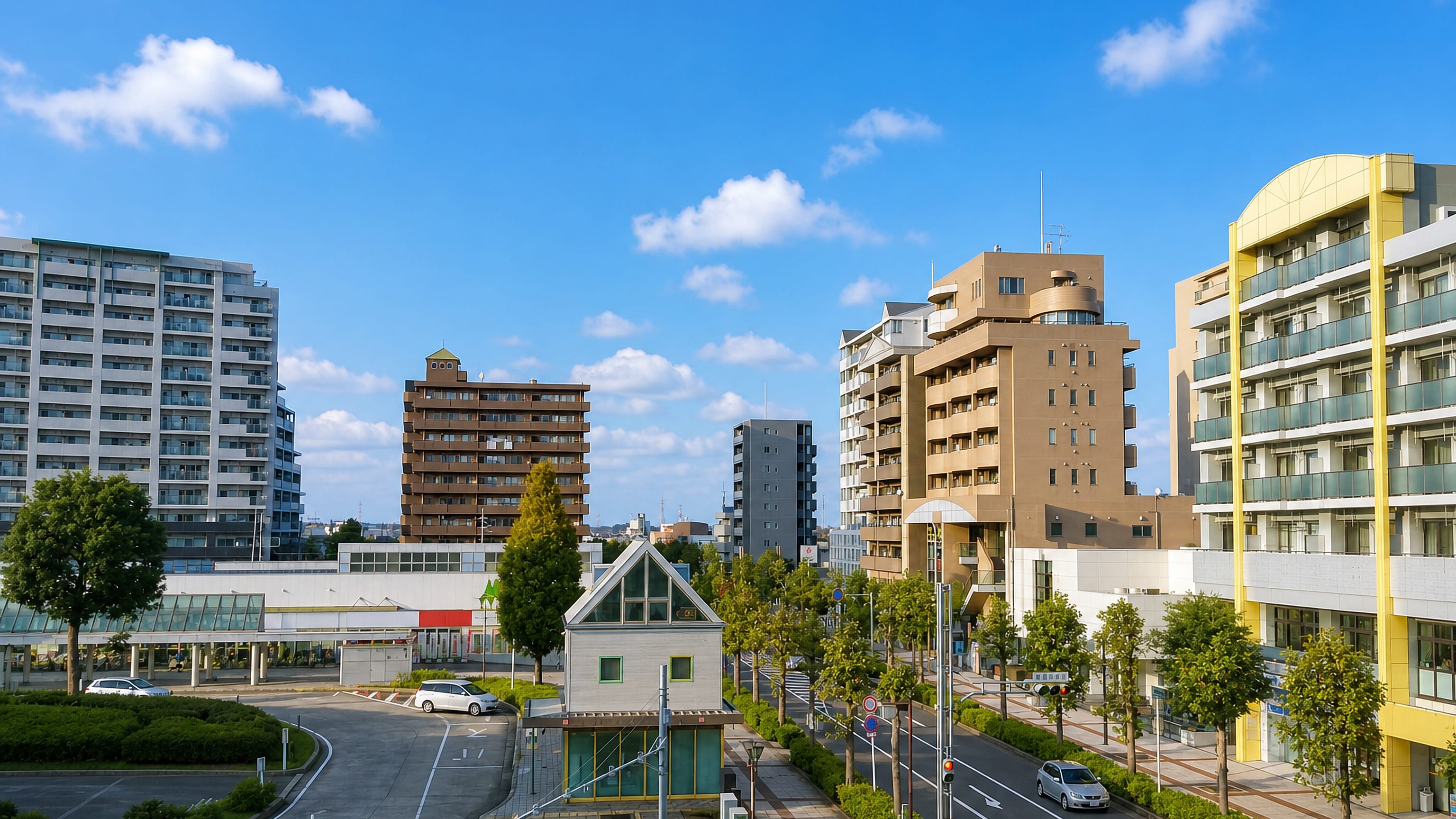 Wide boulevard in Yachiyo, Chiba, lined with mid-rise apartment blocks and shops under a clear sky.