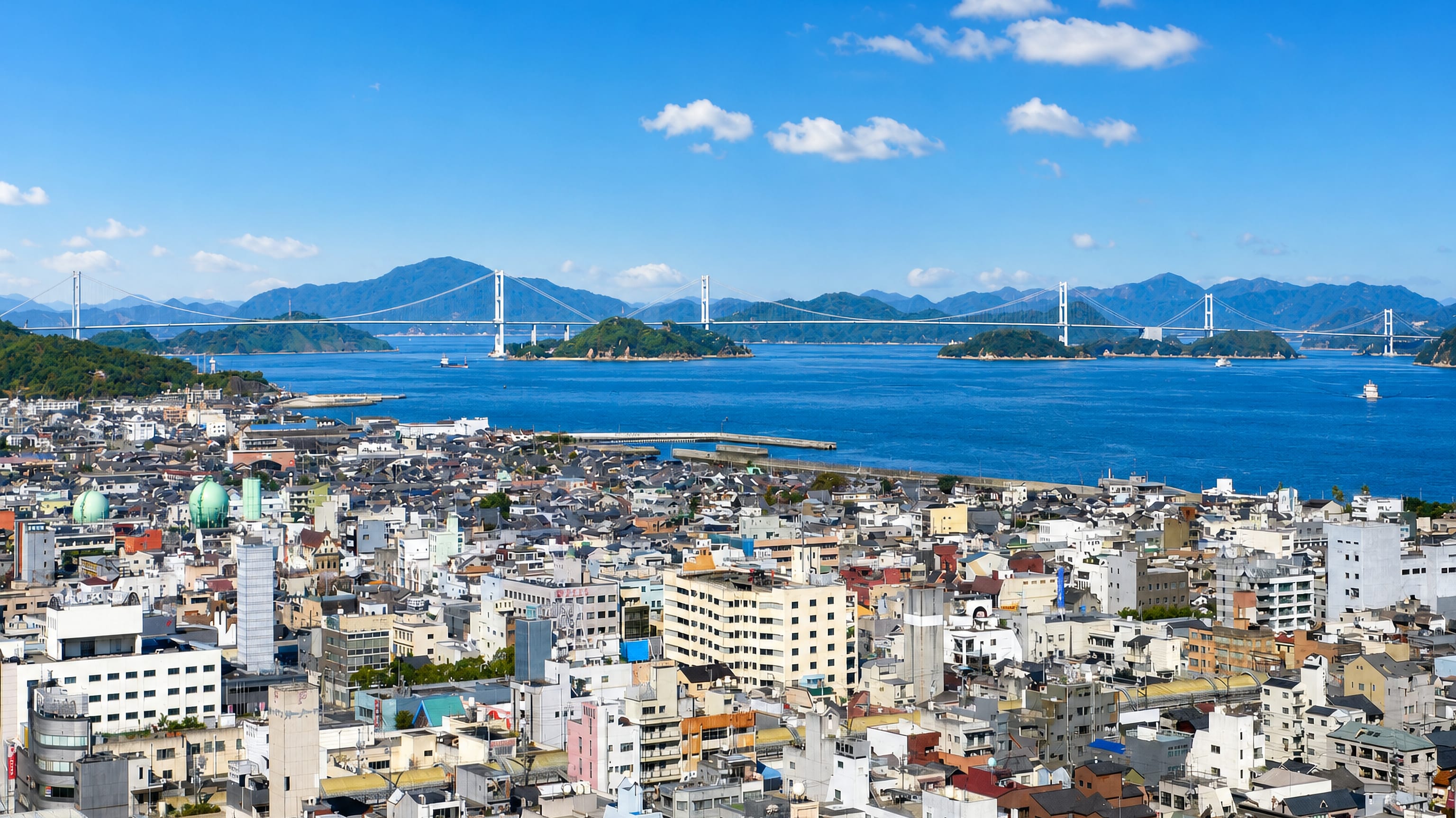 The Kurushima-Kaikyo suspension bridges span the strait beyond the dense rooftops of Imabari, Ehime.