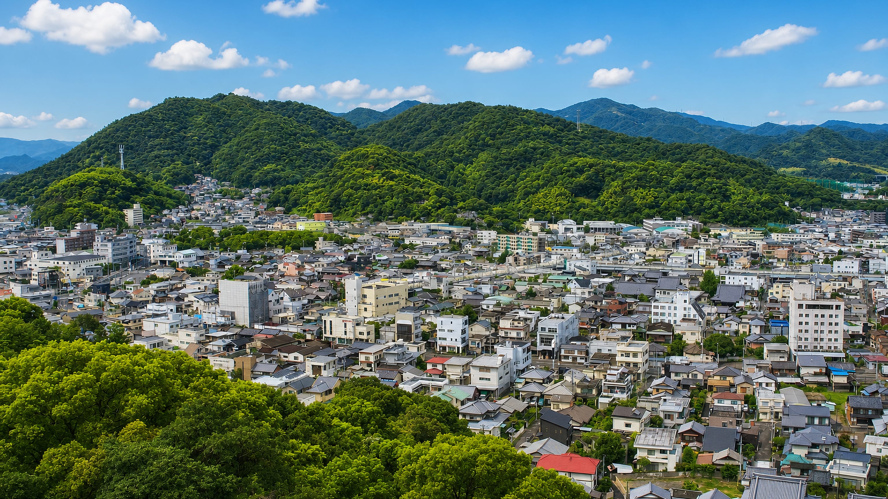Shikokuchūō, Japan, low-rise townscape spreading below forested Ehime mountains on a clear summer day.