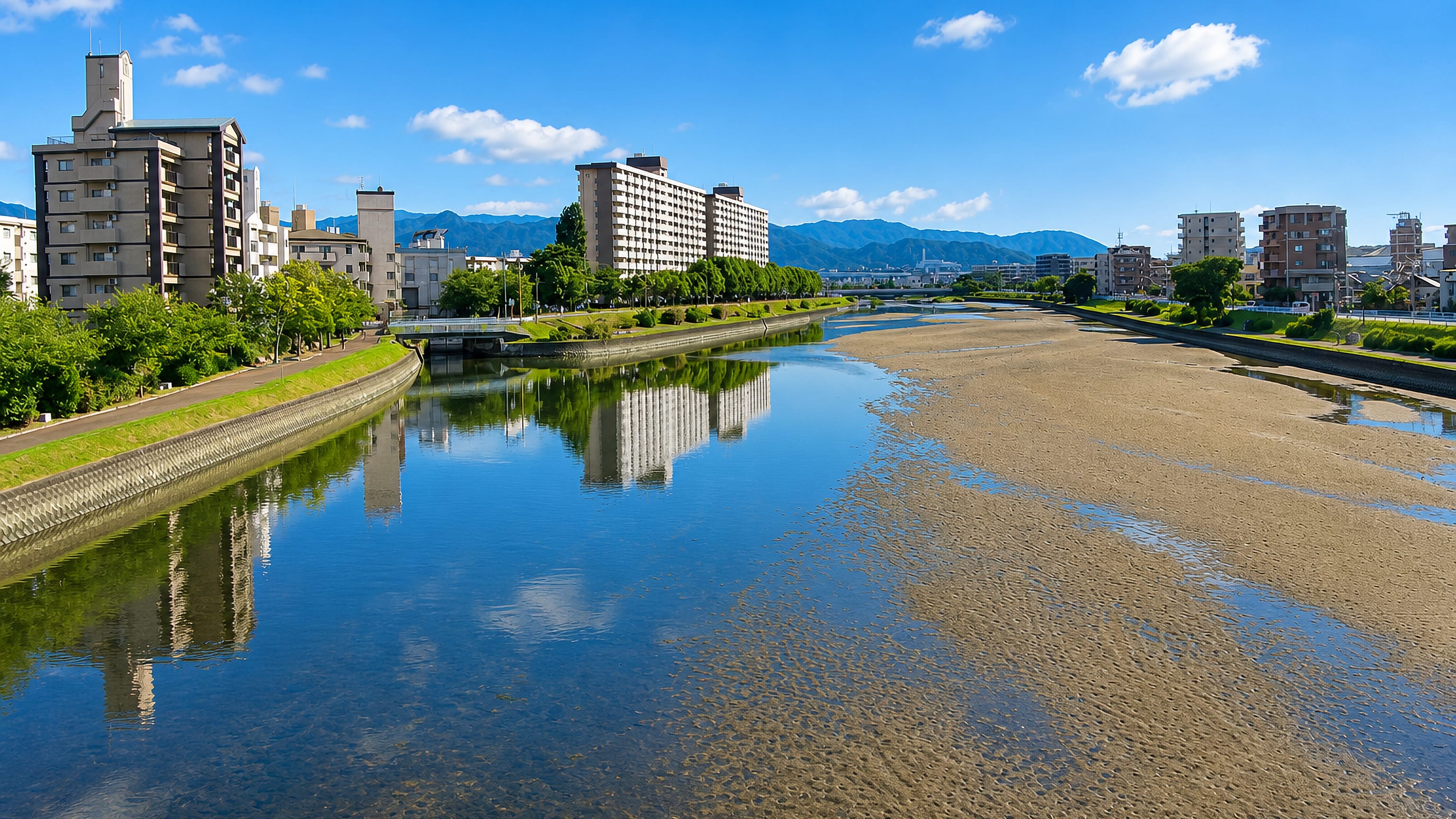 Apartment blocks along a tidal riverbank at Atagominami in Fukuoka, with hills on the horizon.