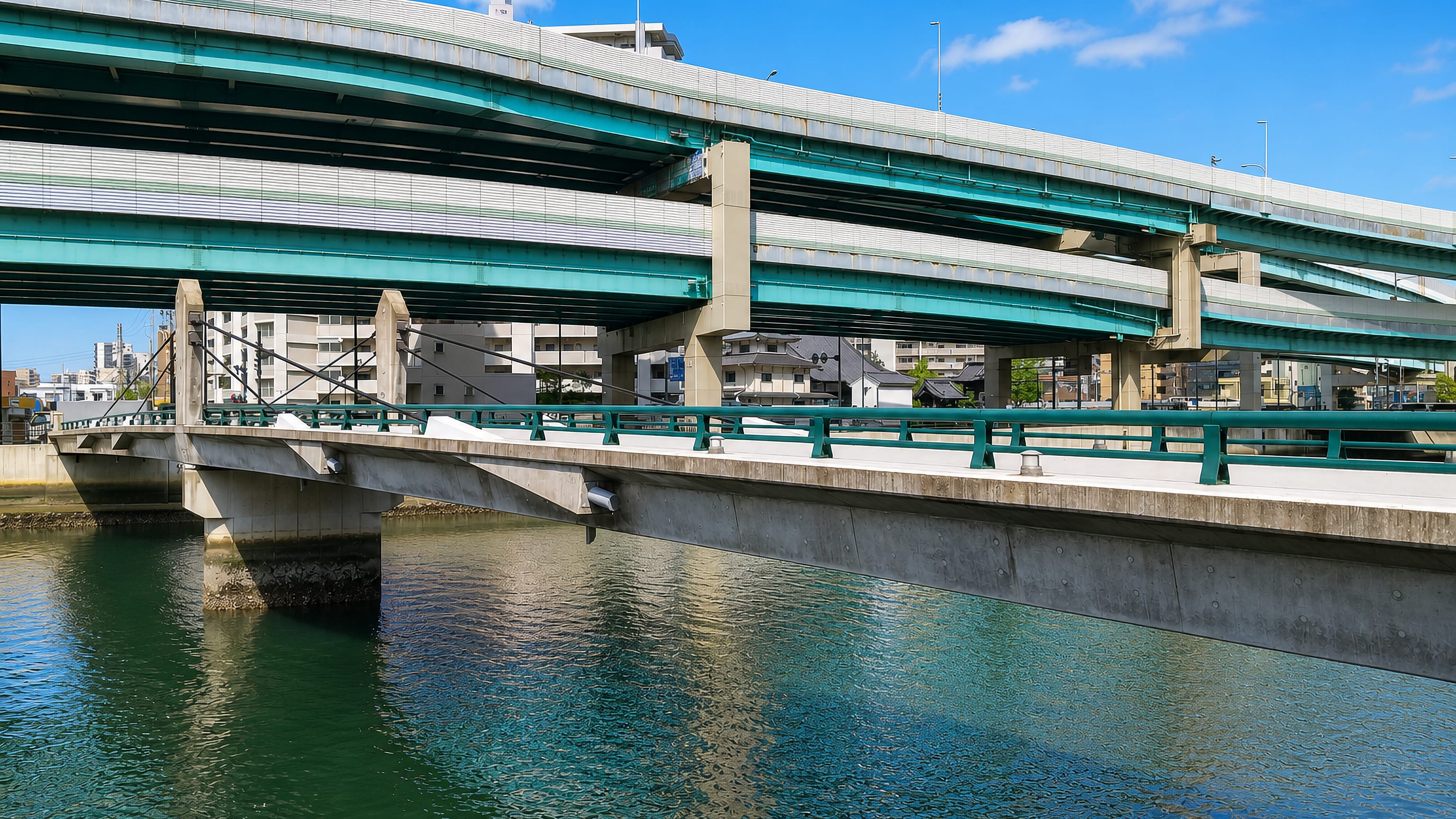 Elevated expressway viaducts crossing the river beside Chiyo, Fukuoka, with apartment blocks behind.