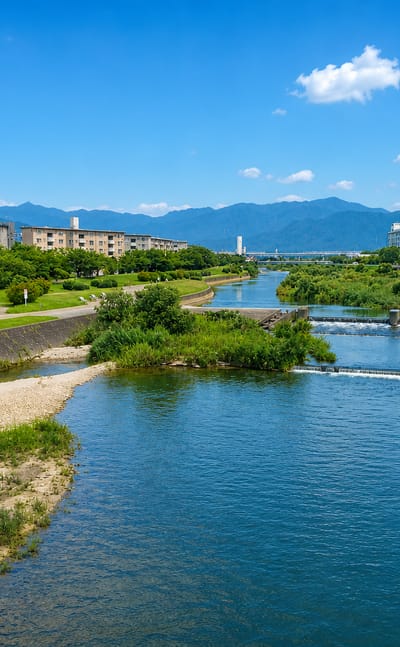 River weirs and grassy embankments below apartment blocks and distant mountains at Fukushige, Fukuoka