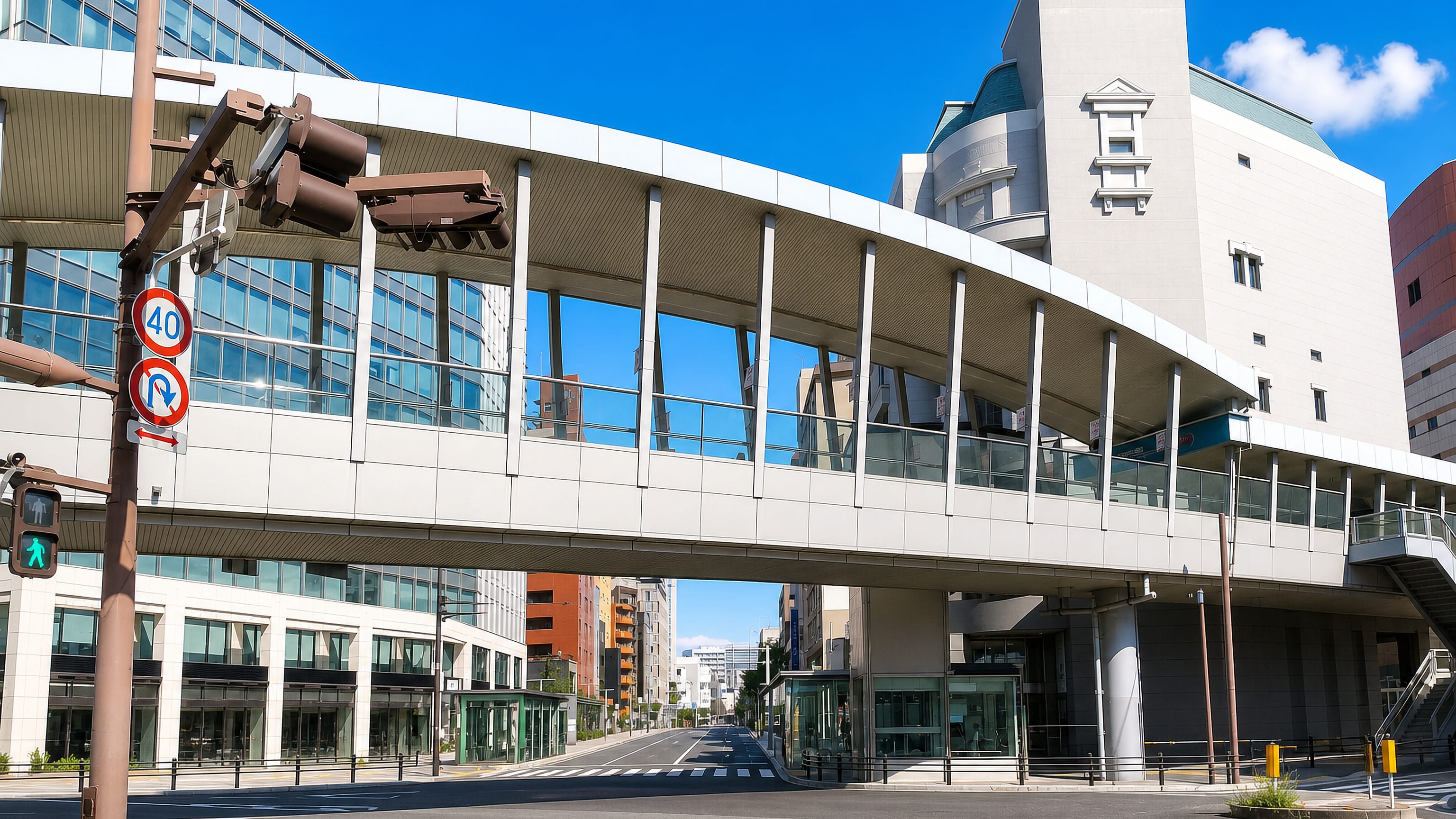 Sunlit street in Gionmachi, Fukuoka, with a curving pedestrian skywalk linking modern glass-fronted buildings.