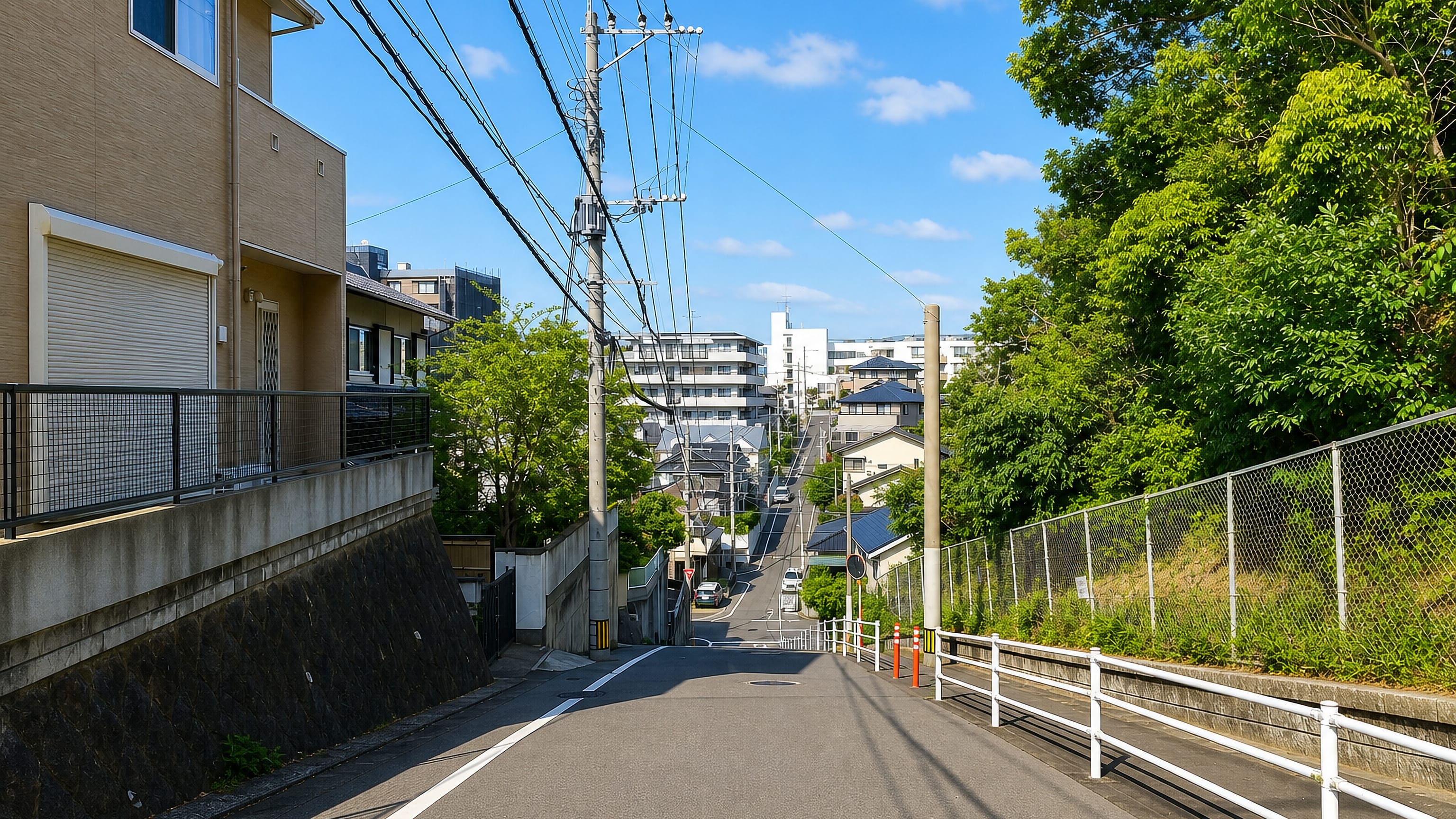 Sloping residential street with apartment blocks and a wooded hillside in Heiwa, Chūō-ku, Fukuoka.