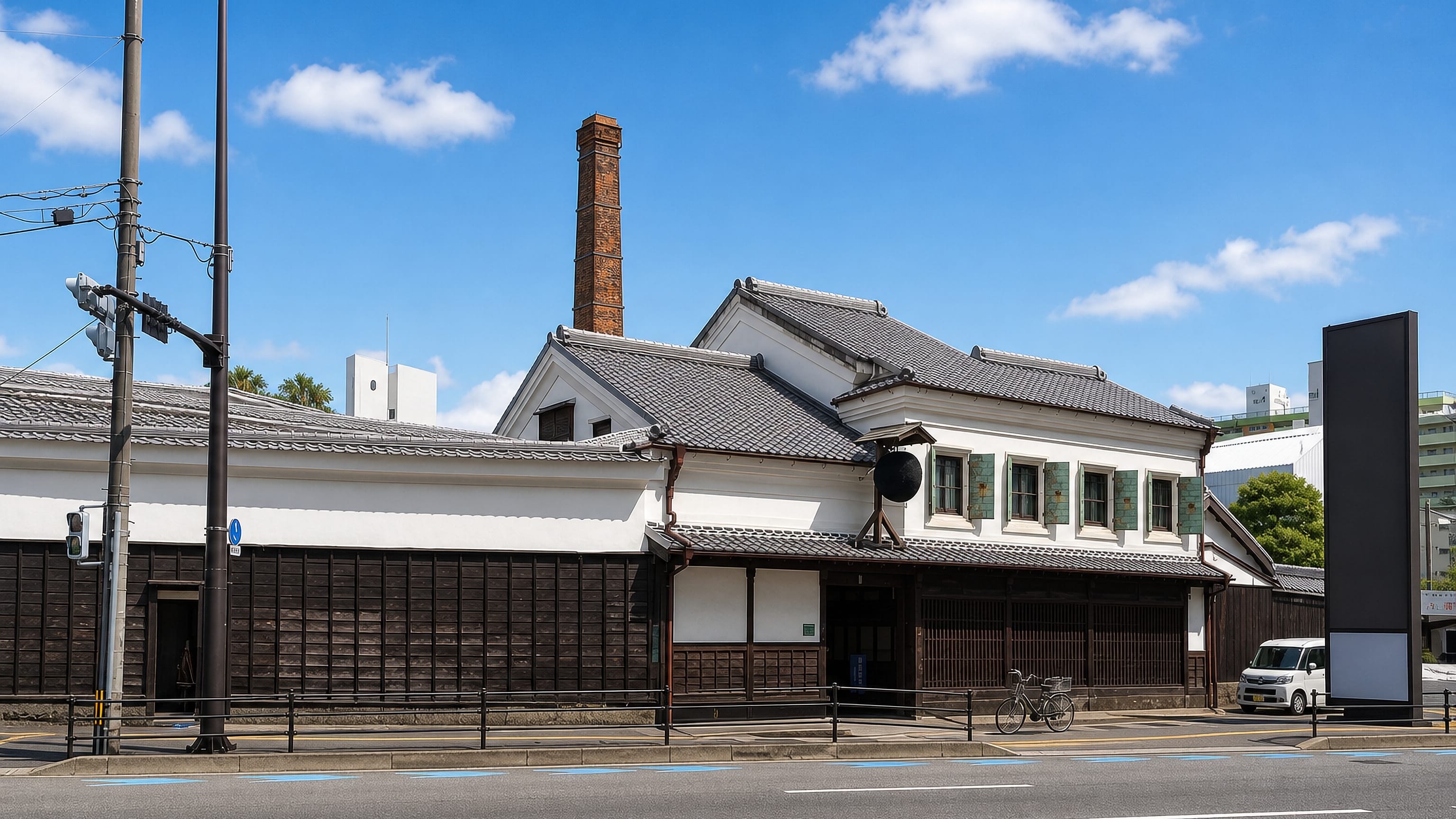 Traditional white-plaster and dark-timber brewery buildings with a brick chimney on a street in Katakasu, Fukuoka.