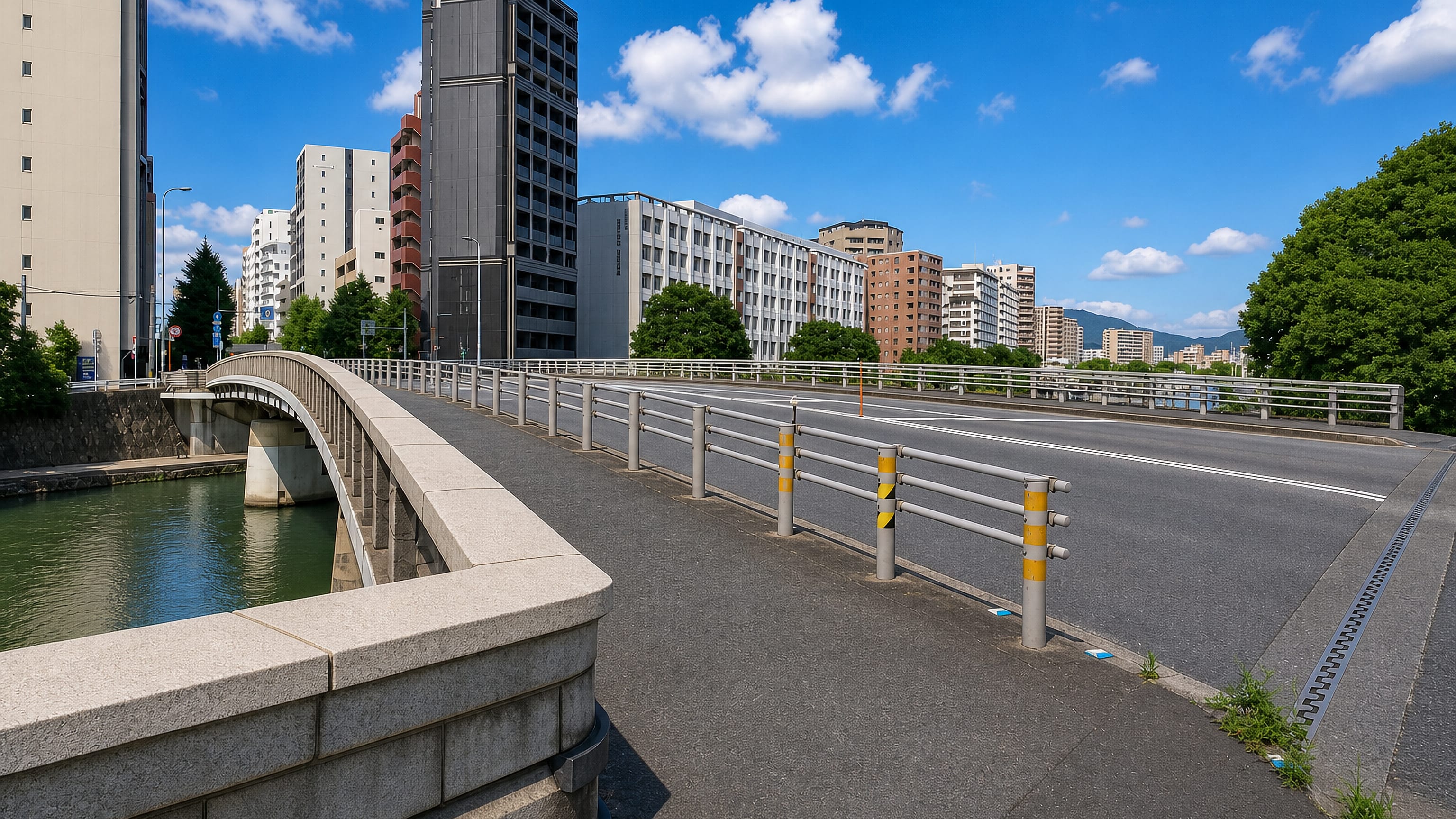 Bridge over a canal beneath mid-rise apartment towers in Minoshima, Fukuoka, with hills on the horizon.