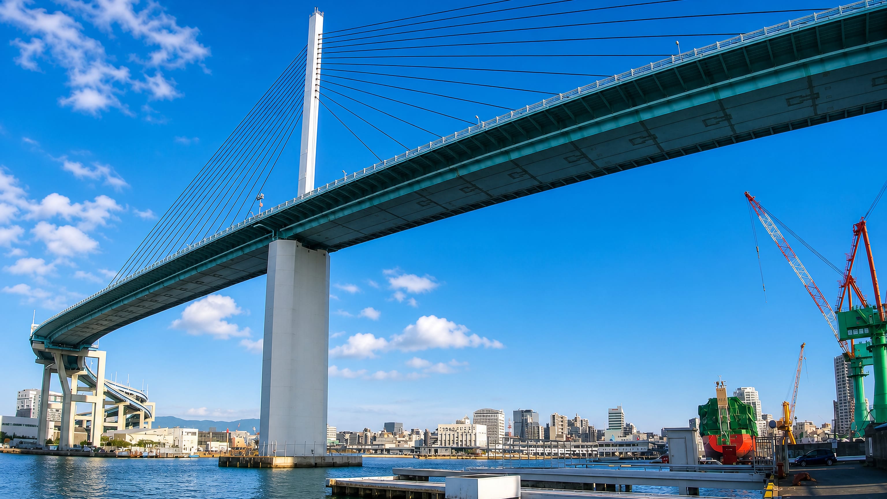 Cable-stayed bridge arcing over the harbour with dockside cranes and city blocks at Nanotsu, Fukuoka.
