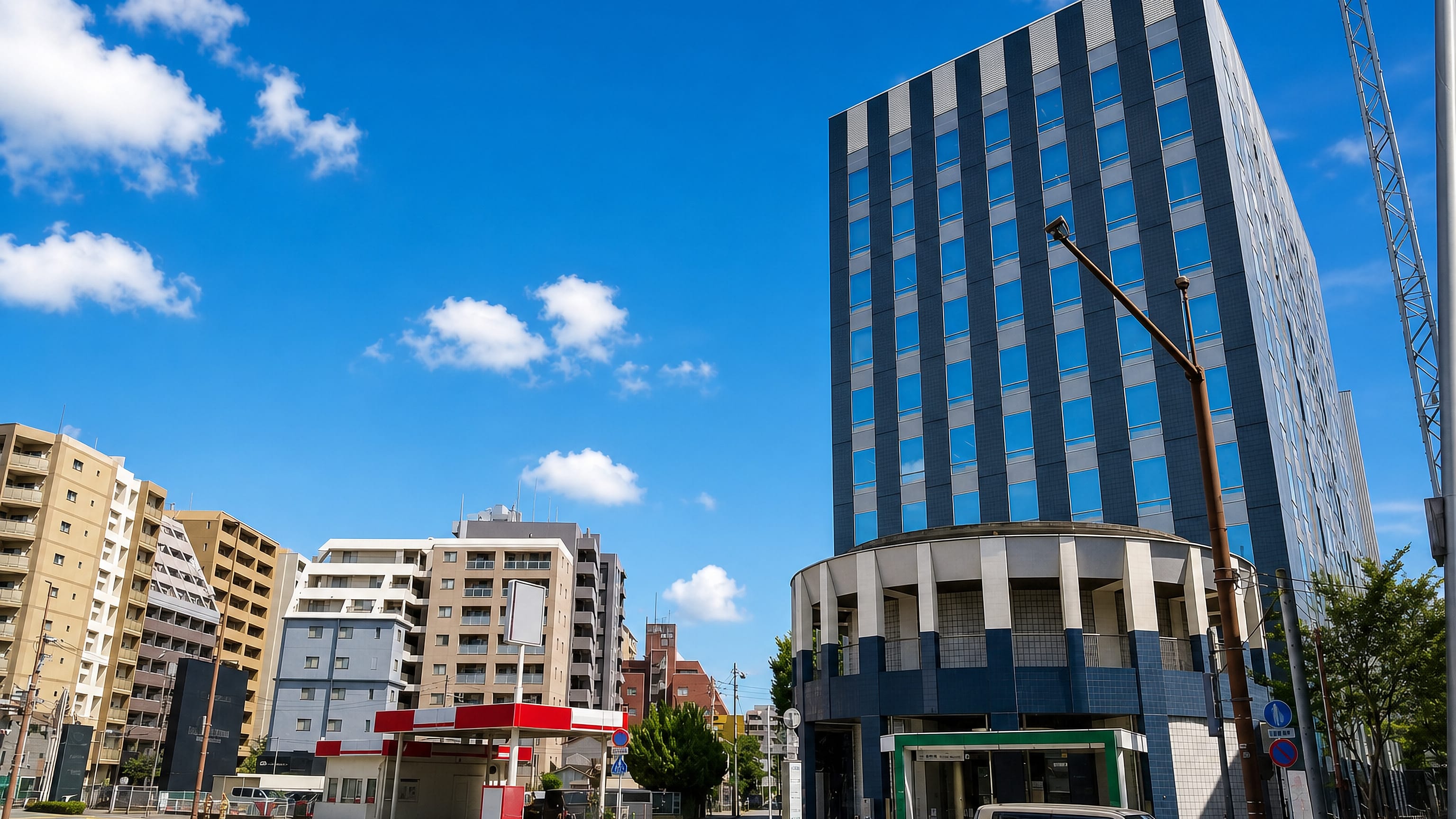 Glass-fronted office tower, apartment blocks and a subway entrance at a street corner in Shirogane, Fukuoka.