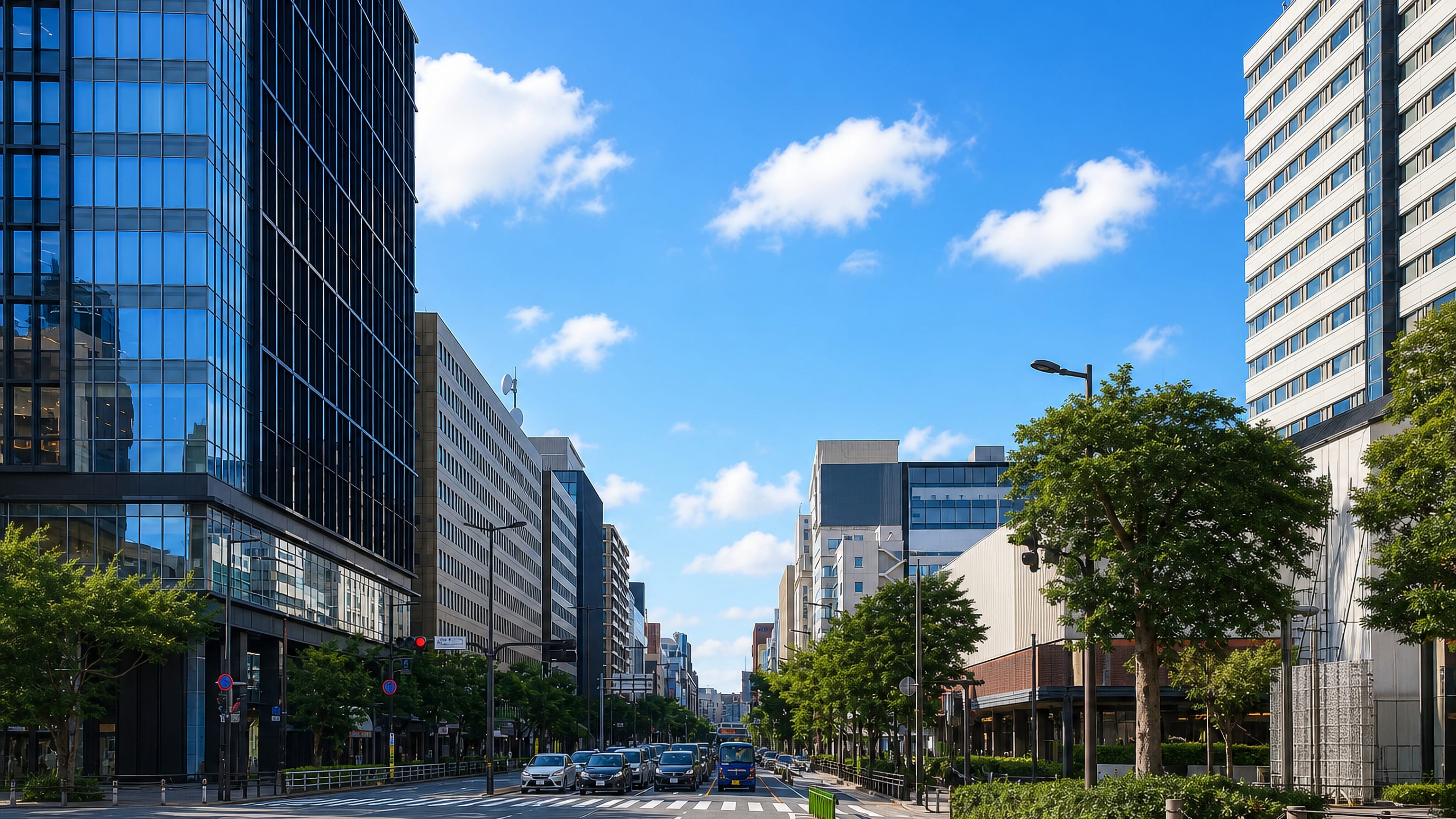 Watanabe-dōri boulevard in Fukuoka, lined with glass office towers and street trees under a clear blue sky.