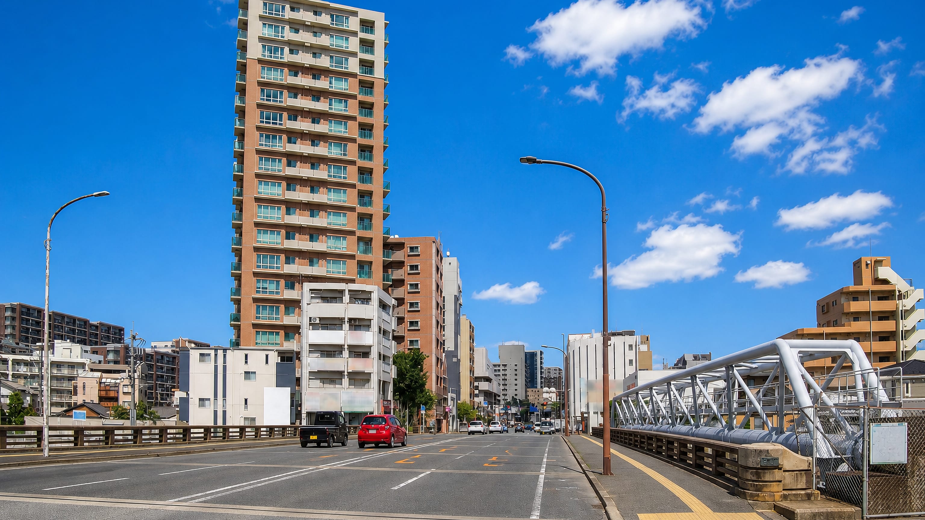 Wide street beside a steel truss bridge and a tall residential tower in Yayoi, Fukuoka.
