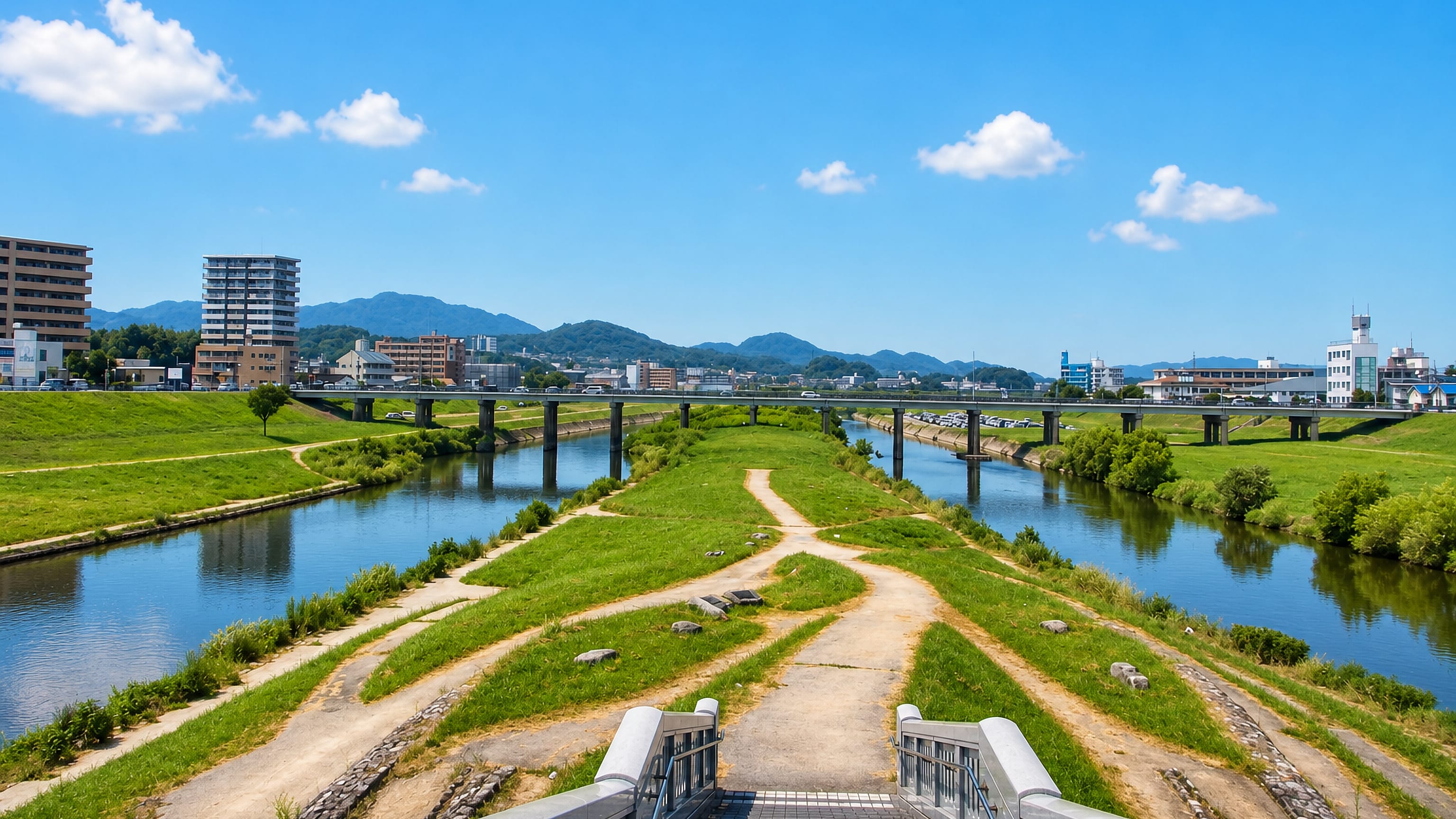The river and grassy embankments running through Iizuka, Japan, with hills and town buildings beyond.