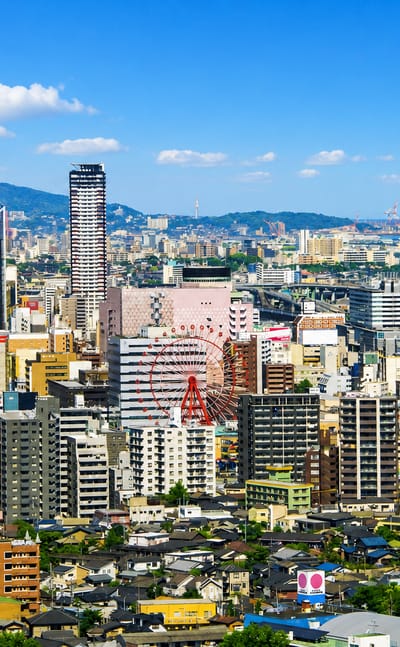 Kitakyushu cityscape in Fukuoka, with a Ferris wheel, a tall dark tower and a pink building among dense blocks.