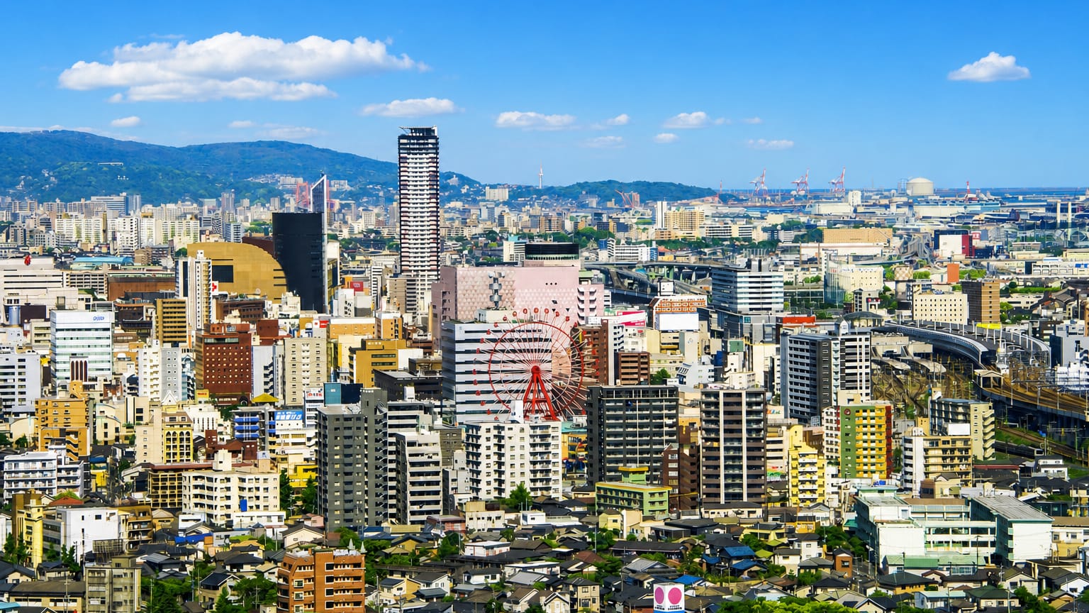Kitakyushu cityscape in Fukuoka, with a Ferris wheel, a tall dark tower and a pink building among dense blocks.
