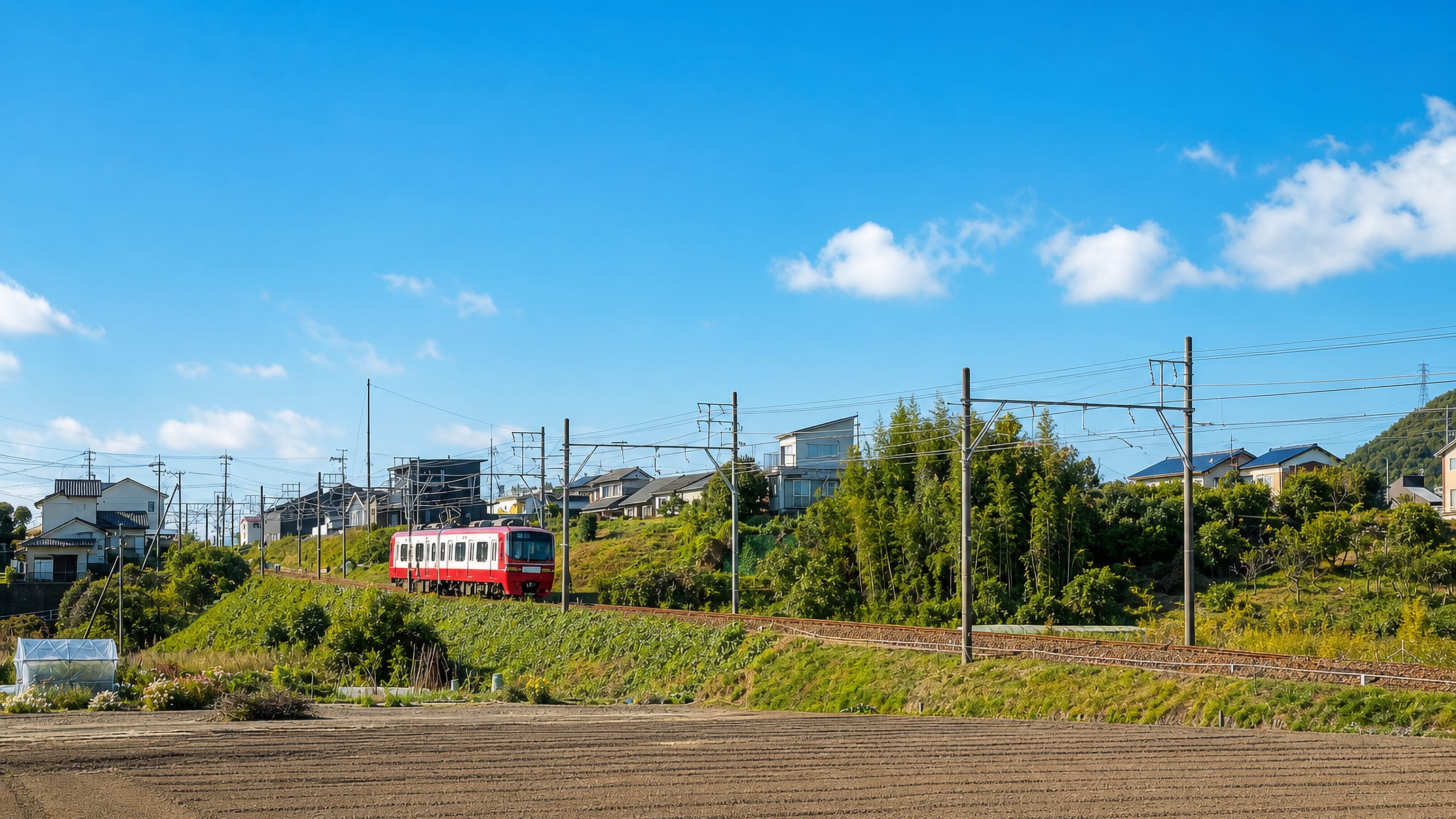 A red Meitetsu train passing hillside houses and farm fields in Kakamigahara, Gifu, Japan.