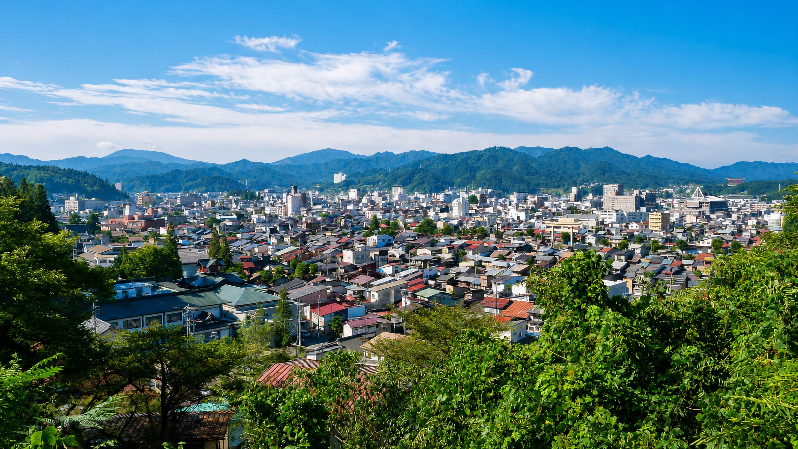 Takayama's low-rise Hida basin rooftops spread below forested mountain ridges, framed by hillside greenery.