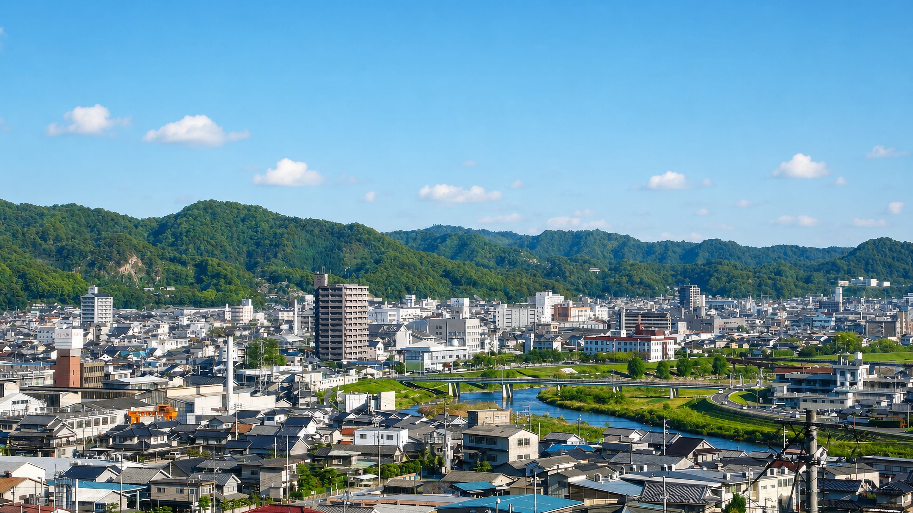 Rooftops and mid-rise blocks of Fuchu, Hiroshima along the river beneath forested hills.