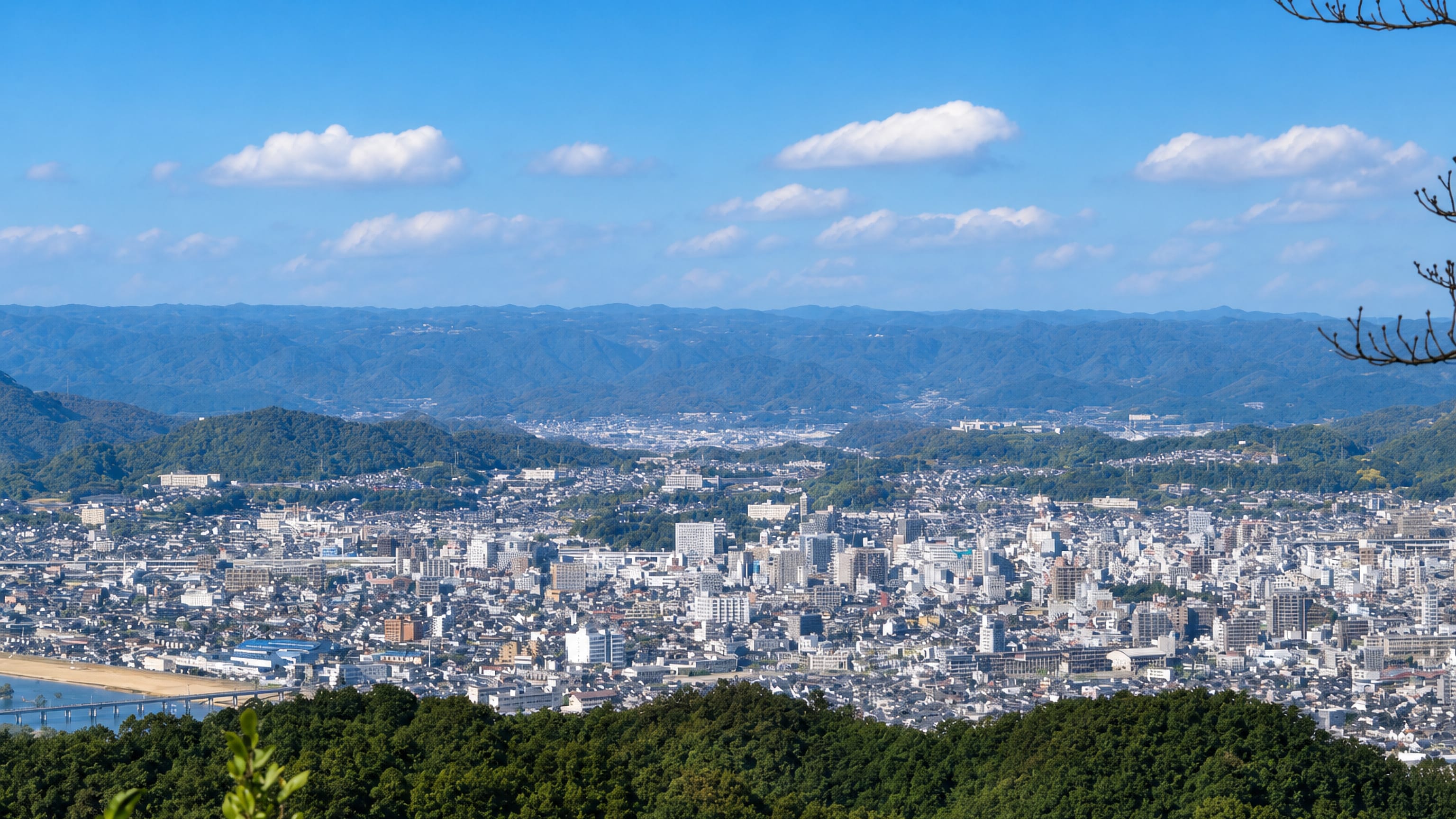 Hilltop panorama over Fukuyama's city centre spread across its river basin and ringed by wooded Hiroshima hills