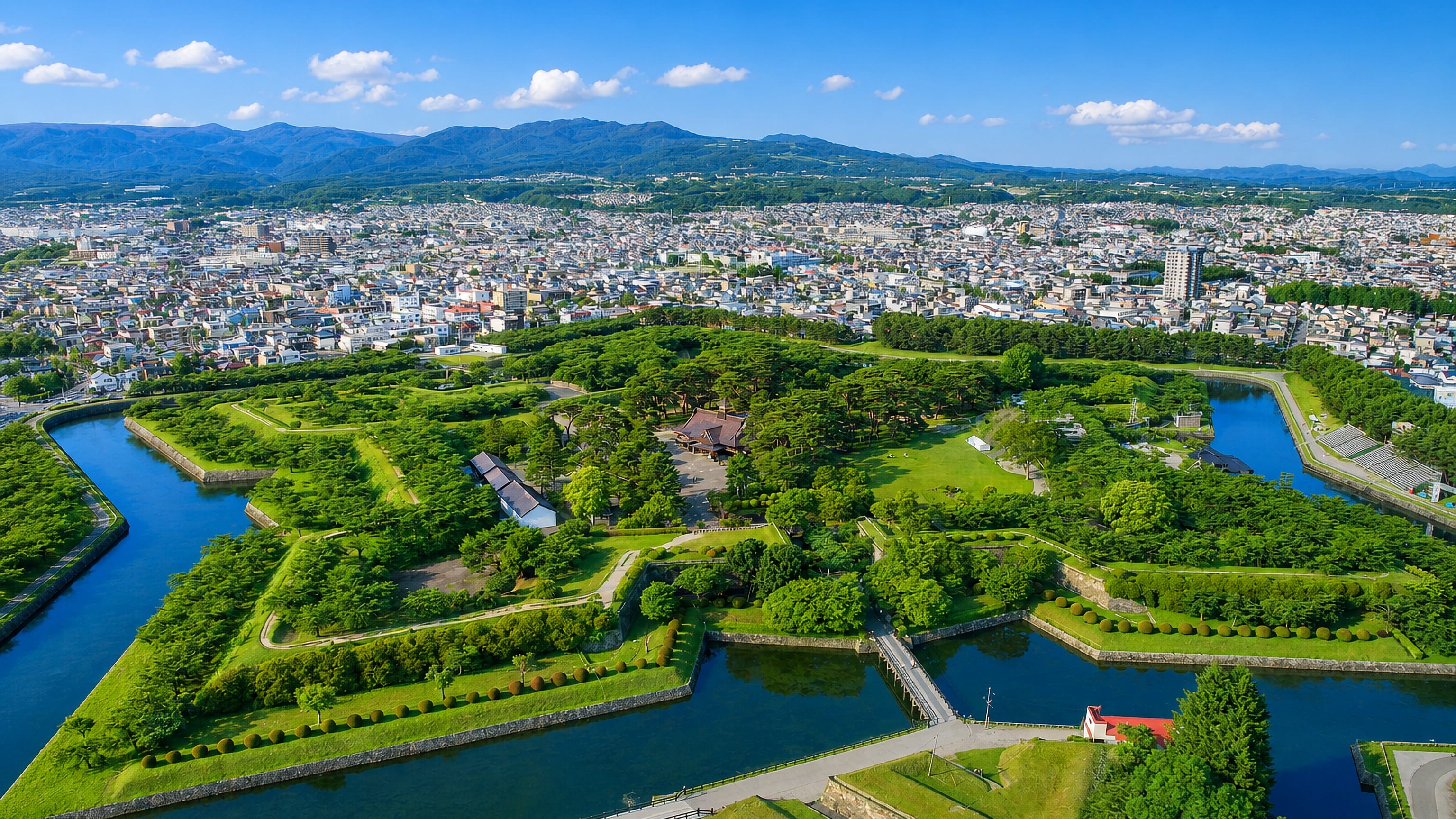 Aerial view of Hakodate's star-shaped Goryokaku fort and moat, with the city and Hokkaido mountains beyond.