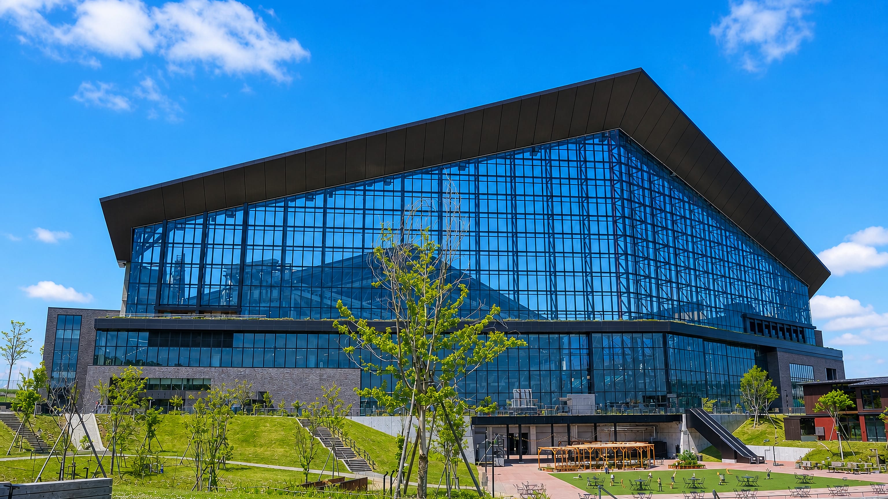 A wide glass-fronted modern hall beside a landscaped park and pond in Kitahiroshima, Hokkaido, Japan.